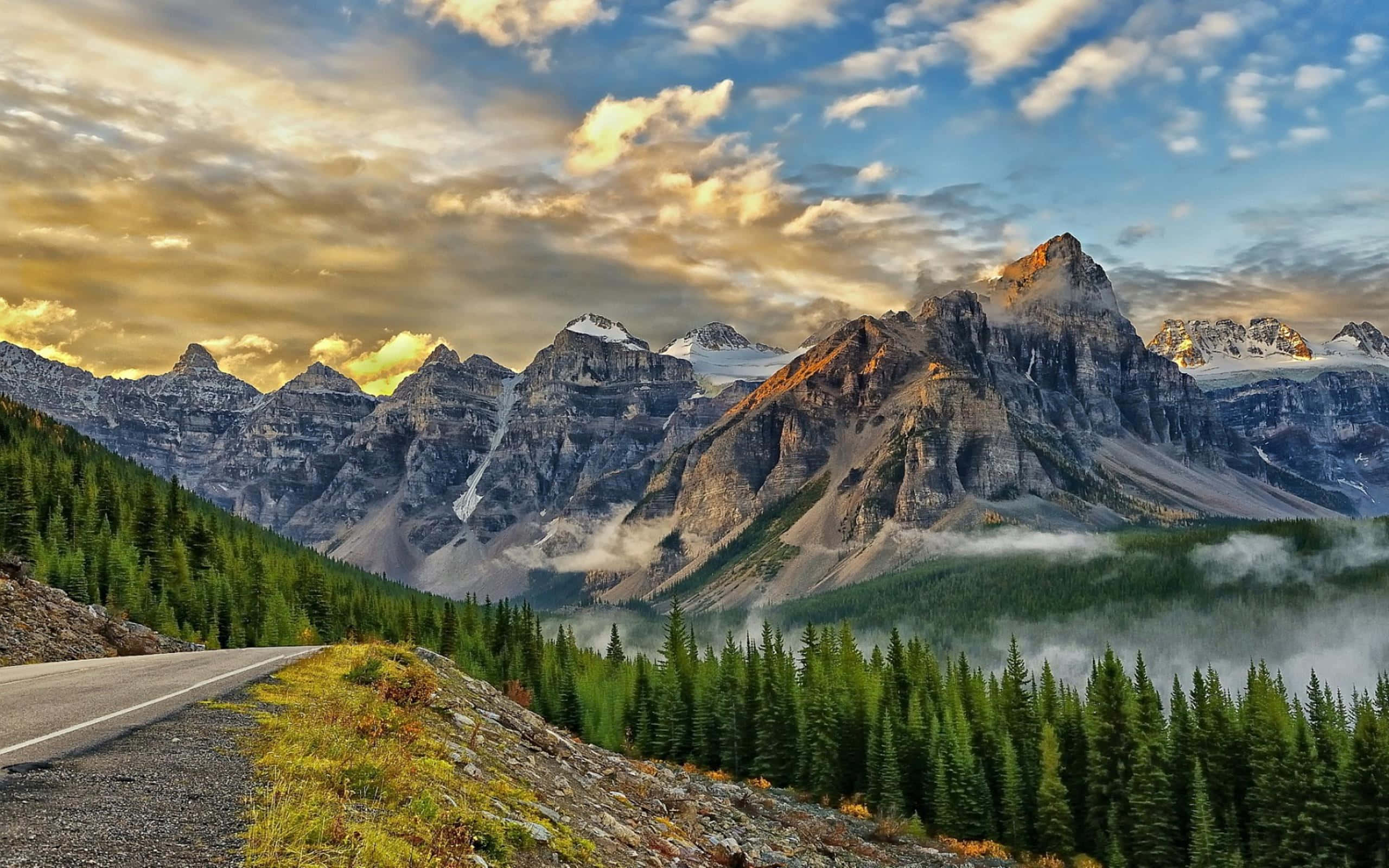 Beautiful Mountain 桌布 壁紙 — 一條蜿蜒的道路穿過迷霧森林，通往沐浴在金色日落光芒中的高聳雪山。
