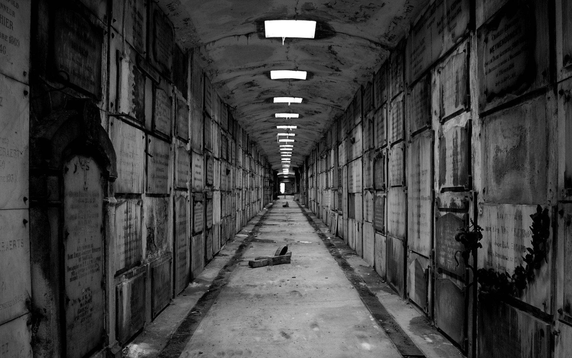 嚇人 桌布 壁紙 — 一條被遺忘的墓園中燈光昏暗的長廊，兩旁排列著風化的墓碑和閃爍的吊燈。