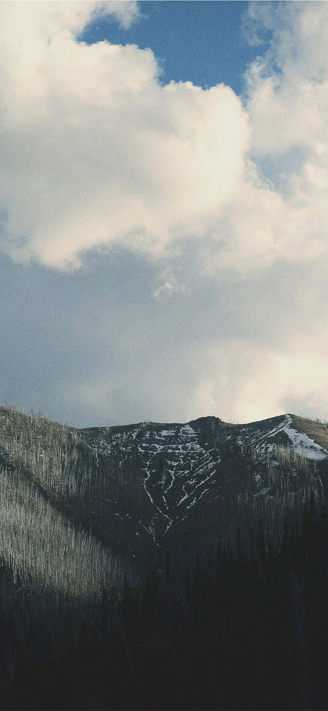 iPhone X Nature 桌布 壁紙 — 一條被雪覆蓋的山脊在佈滿柔和白雲的廣闊天空下升起。