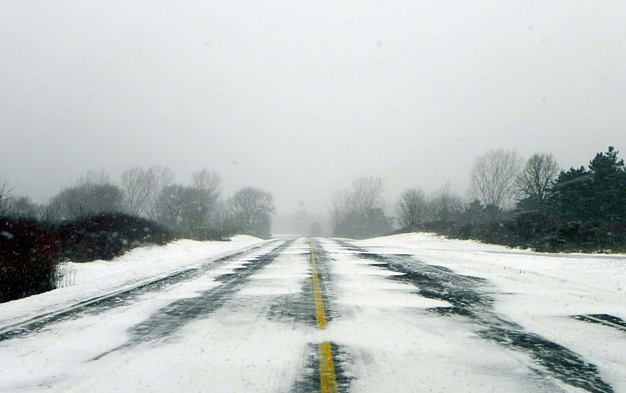 Icy Road 桌布 壁紙 — 一條被雪覆蓋的道路延伸至霧氣瀰漫的冬季景觀，兩旁是光禿禿的樹木。