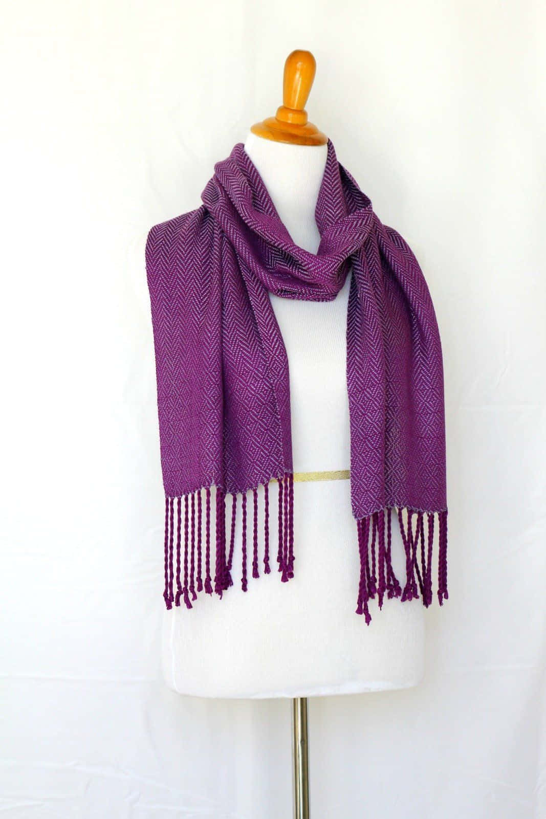 Purple Scarf 桌布 壁紙 — 一條豐富的紫色人字紋圍巾，帶有流蘇，優雅地披在白色人體模型上，背景是潔淨的白色。