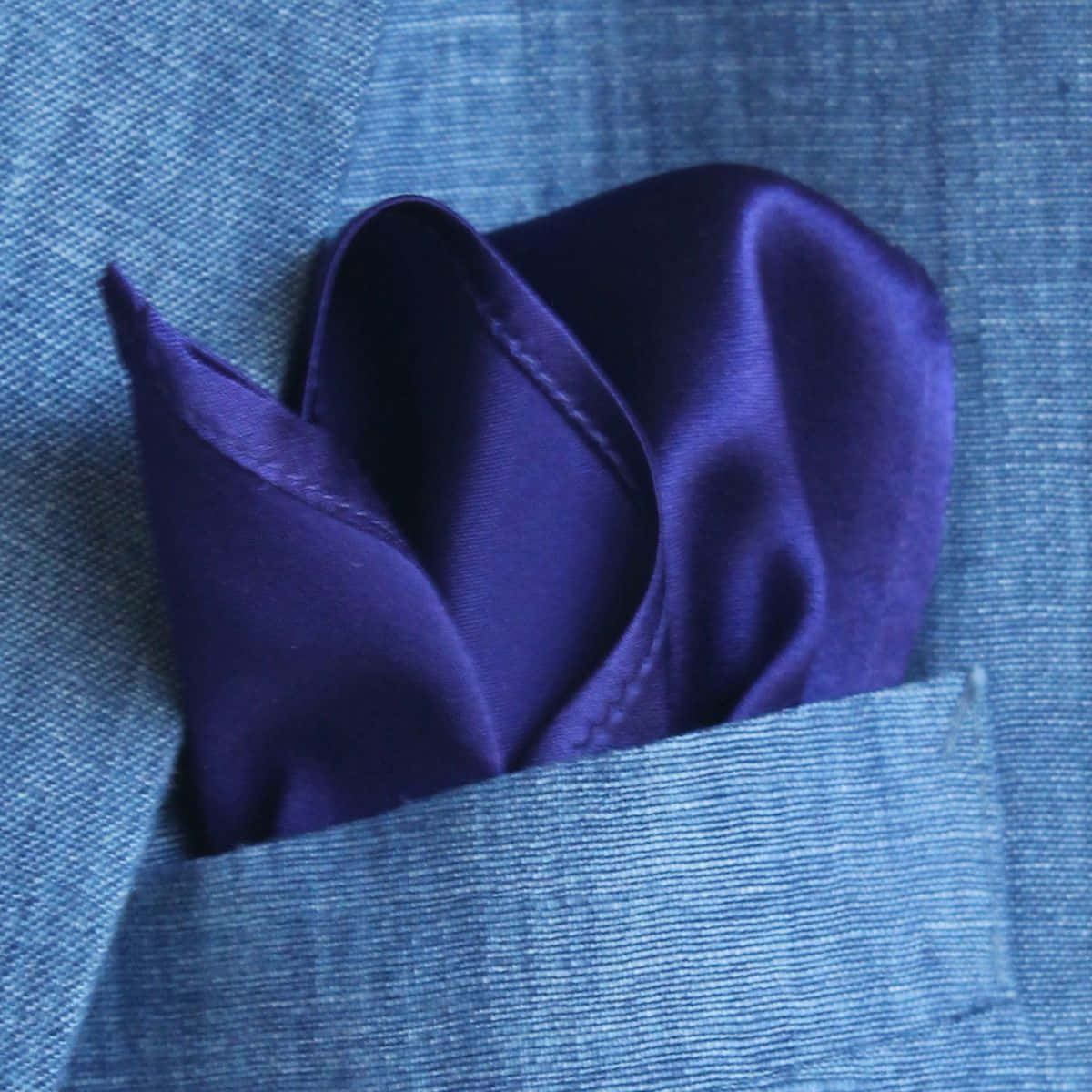 Purple Satin 桌布 壁紙 — 一條質感豐富的紫色緞面口袋方巾，優雅地摺疊在質感藍色西裝外套口袋中。