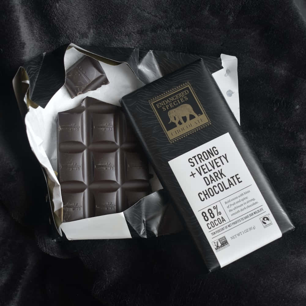 Dark Chocolate 桌布 壁紙 — 一條部分包裝的88%黑朱古力棒放在柔軟的黑色布料上，展現其豐富的質感和大膽的標籤。