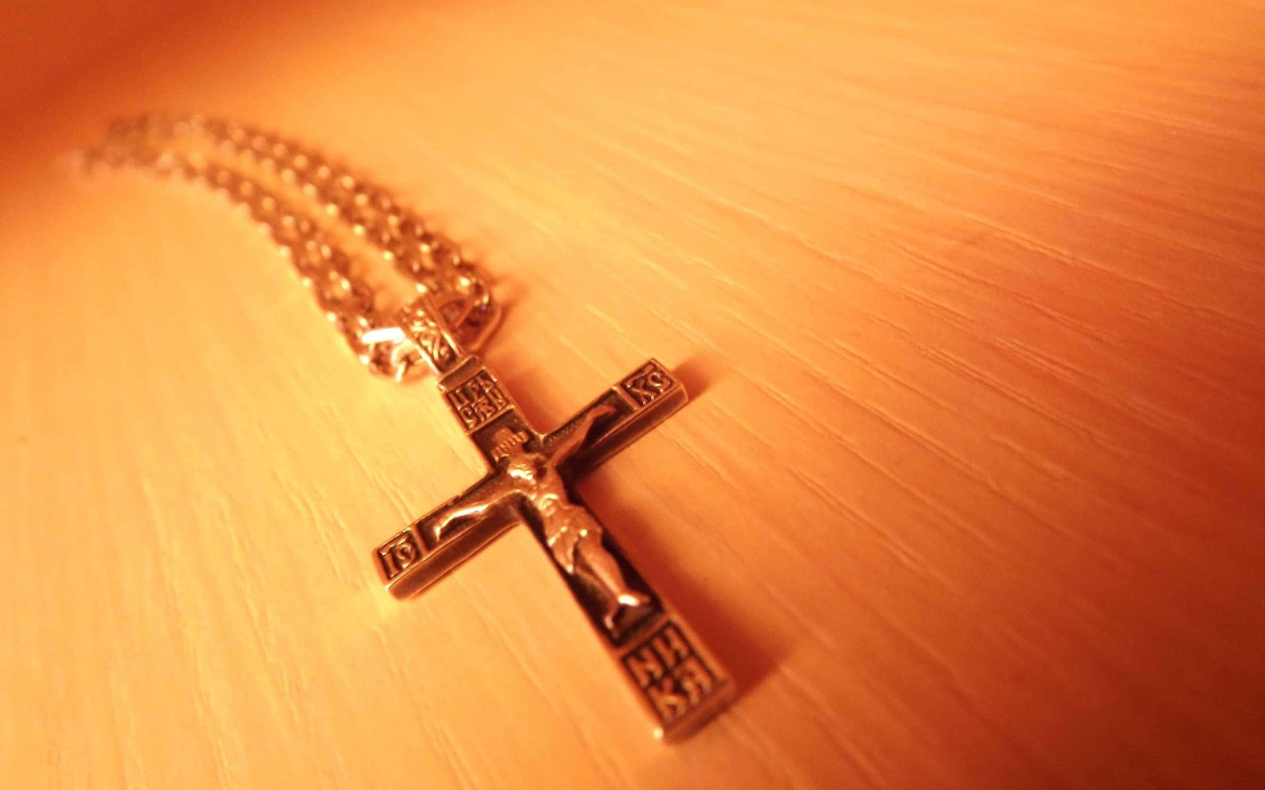 Theology 桌布 壁紙 — 一條金色十字架項鍊放在溫暖的木質表面上，沐浴在柔和的琥珀色光線中。