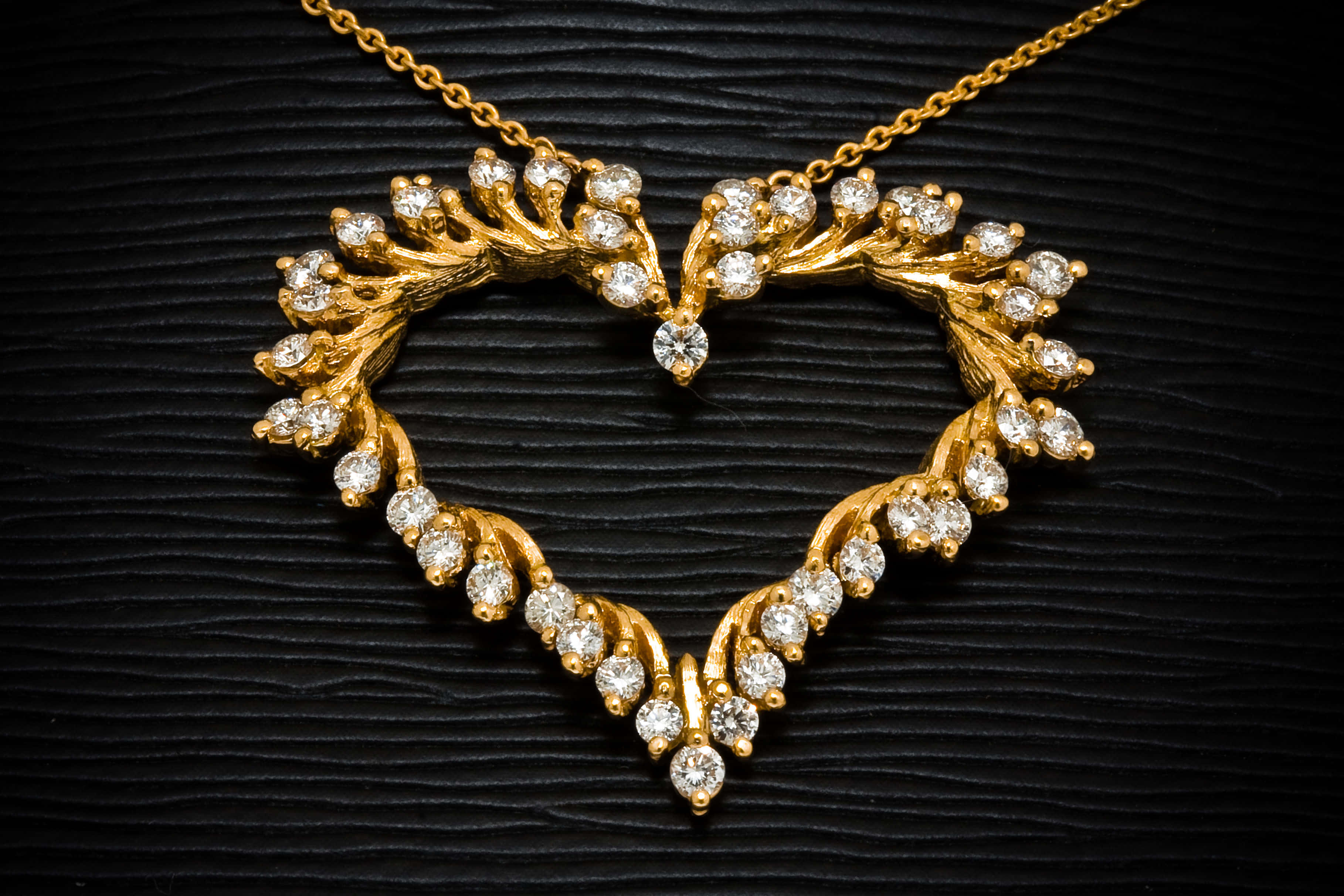 Jewelry Design 桌布 壁紙 — 一條金色心形項鍊，鑲嵌閃爍鑽石，優雅地放置在帶有紋理的黑色表面上。
