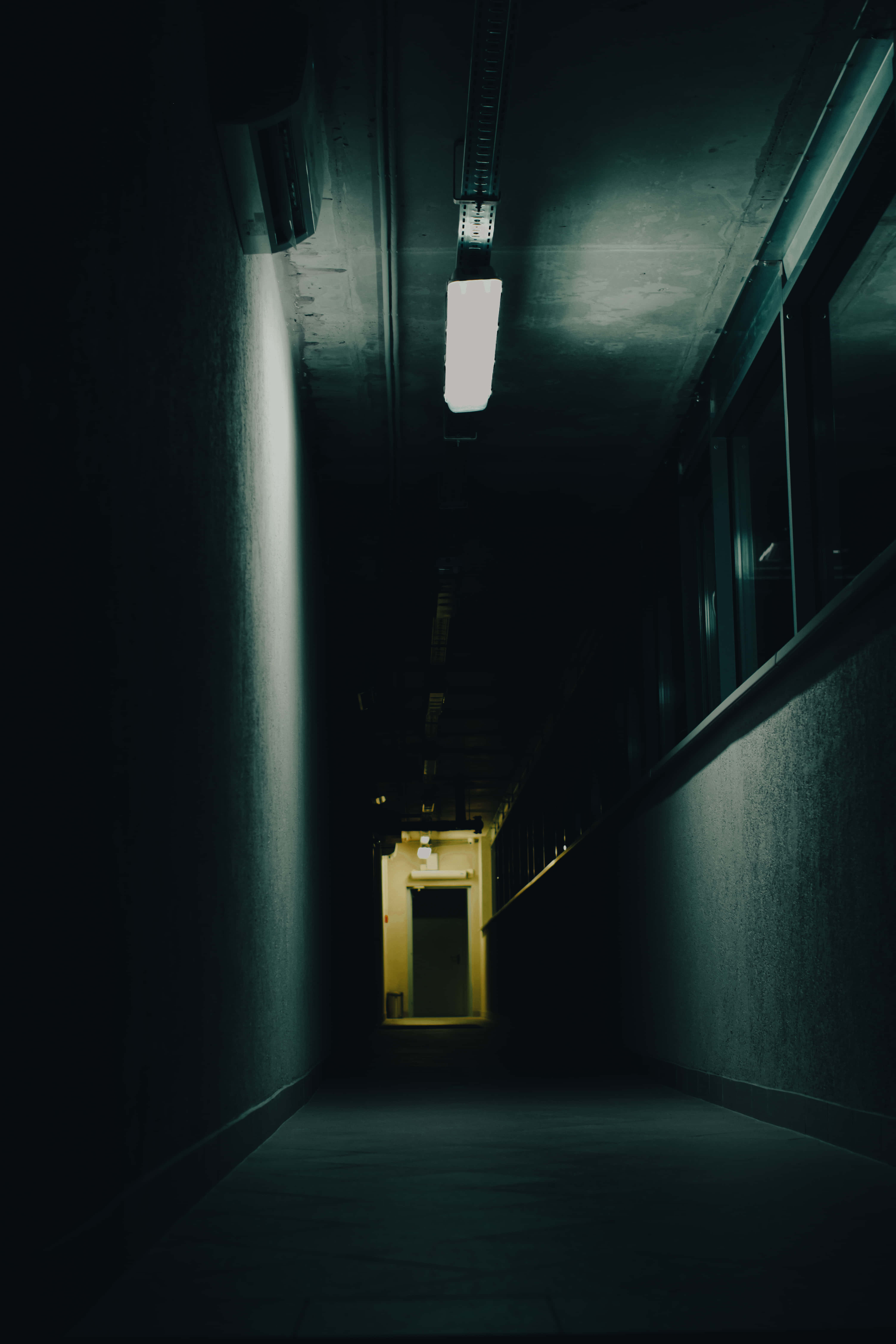 Dark Underground 桌布 壁紙 — 一條長長的昏暗走廊，只有一支螢光燈向遠處的門口投射出詭異的影子。