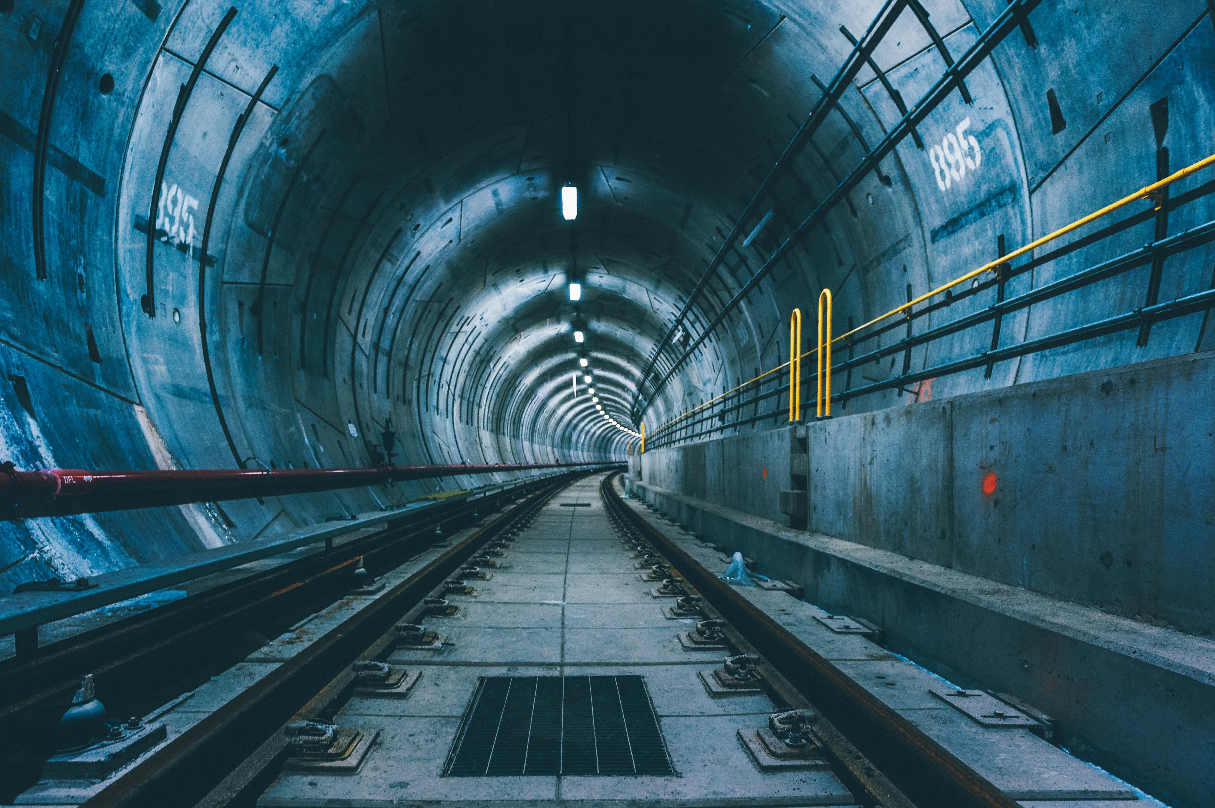 Subway 桌布 壁紙 — 一條長長的混凝土地鐵隧道，鋼軌在冷藍色燈光下延伸至遠方。
