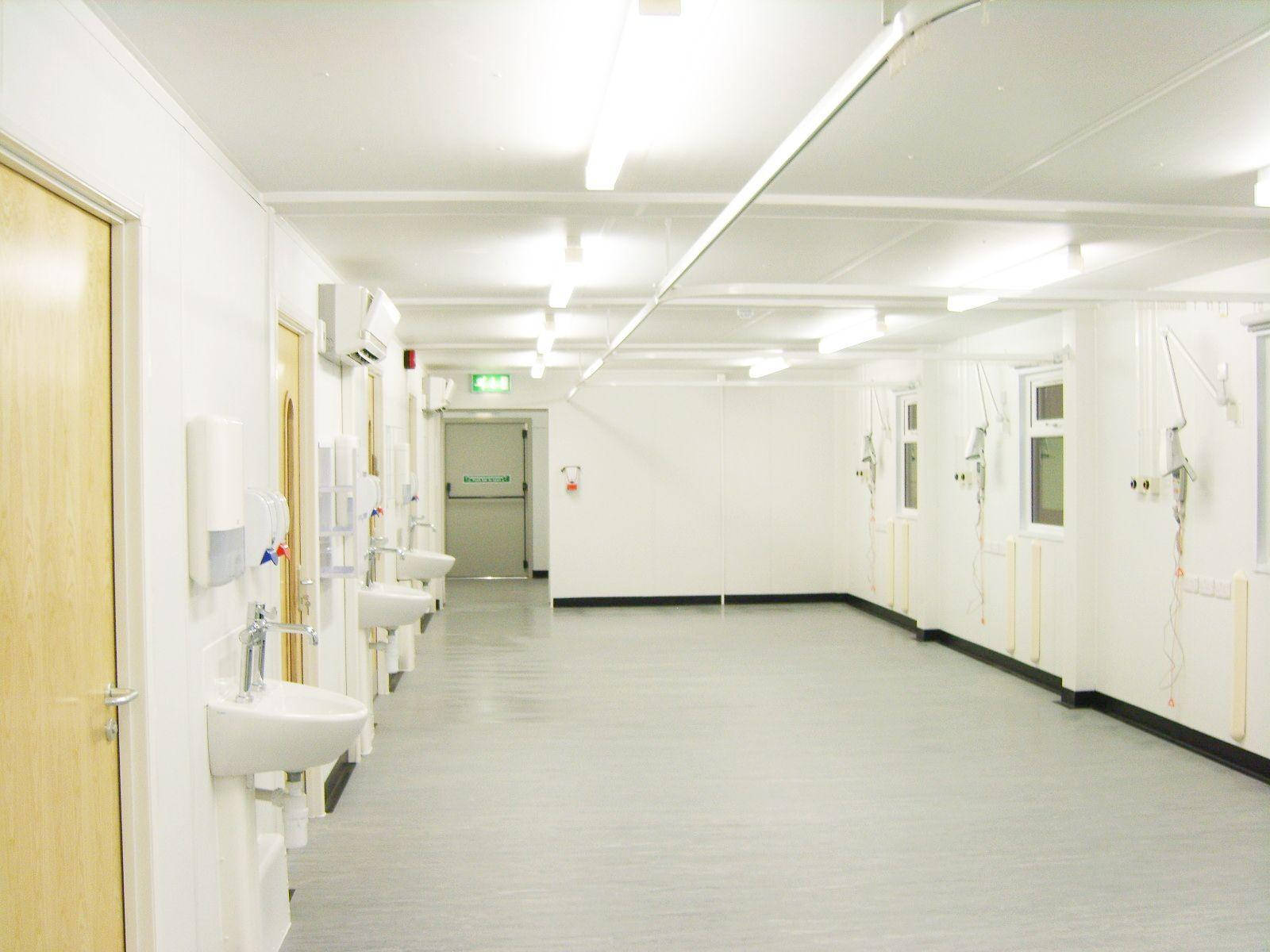 hallway 桌布 壁紙 — 一條長長的無菌醫院走廊，白色牆壁、洗手盆和醫療設備在明亮的螢光燈下。