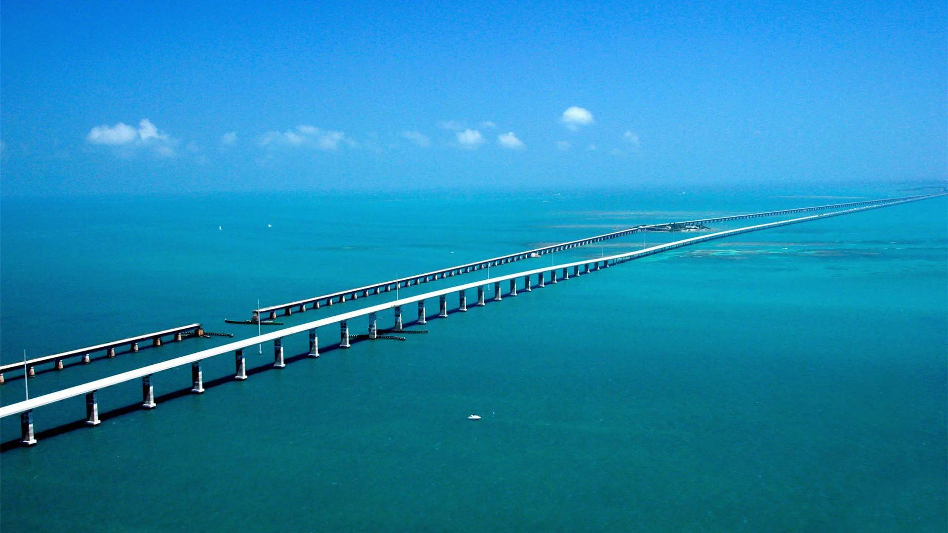 florida 桌布 壁紙 — 一條長長的白色橋樑橫跨在碧綠色的海洋上，天空湛藍，白雲點綴。