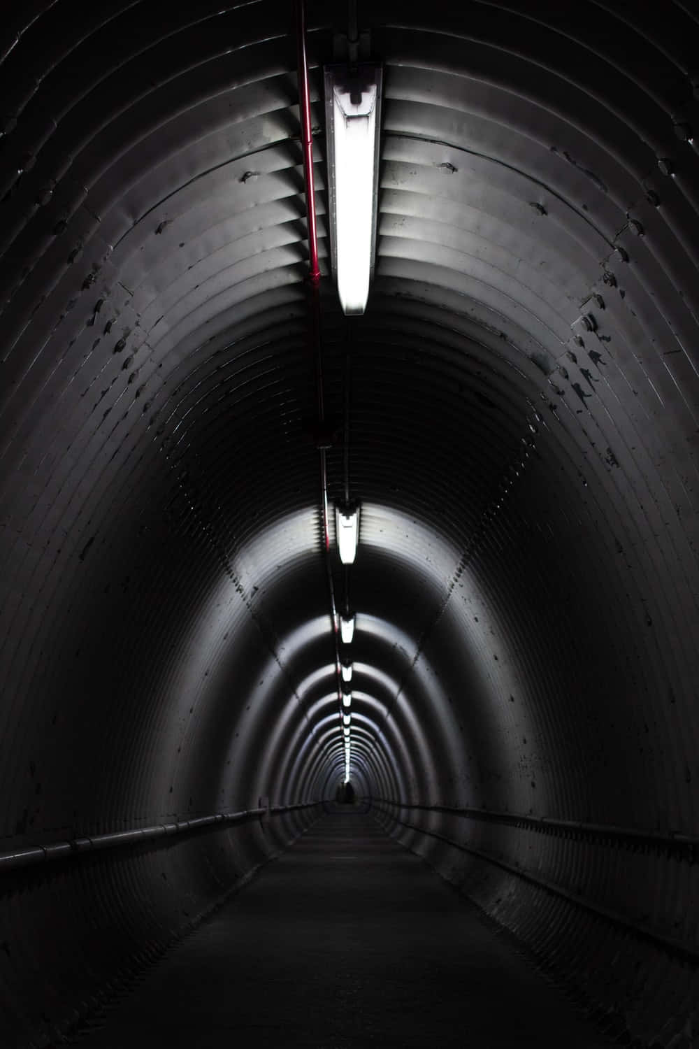 Dark Underground 桌布 壁紙 — 一條長長的黑暗隧道，帶有彎曲的金屬牆壁和明亮的螢光燈，逐漸消失在遠方。