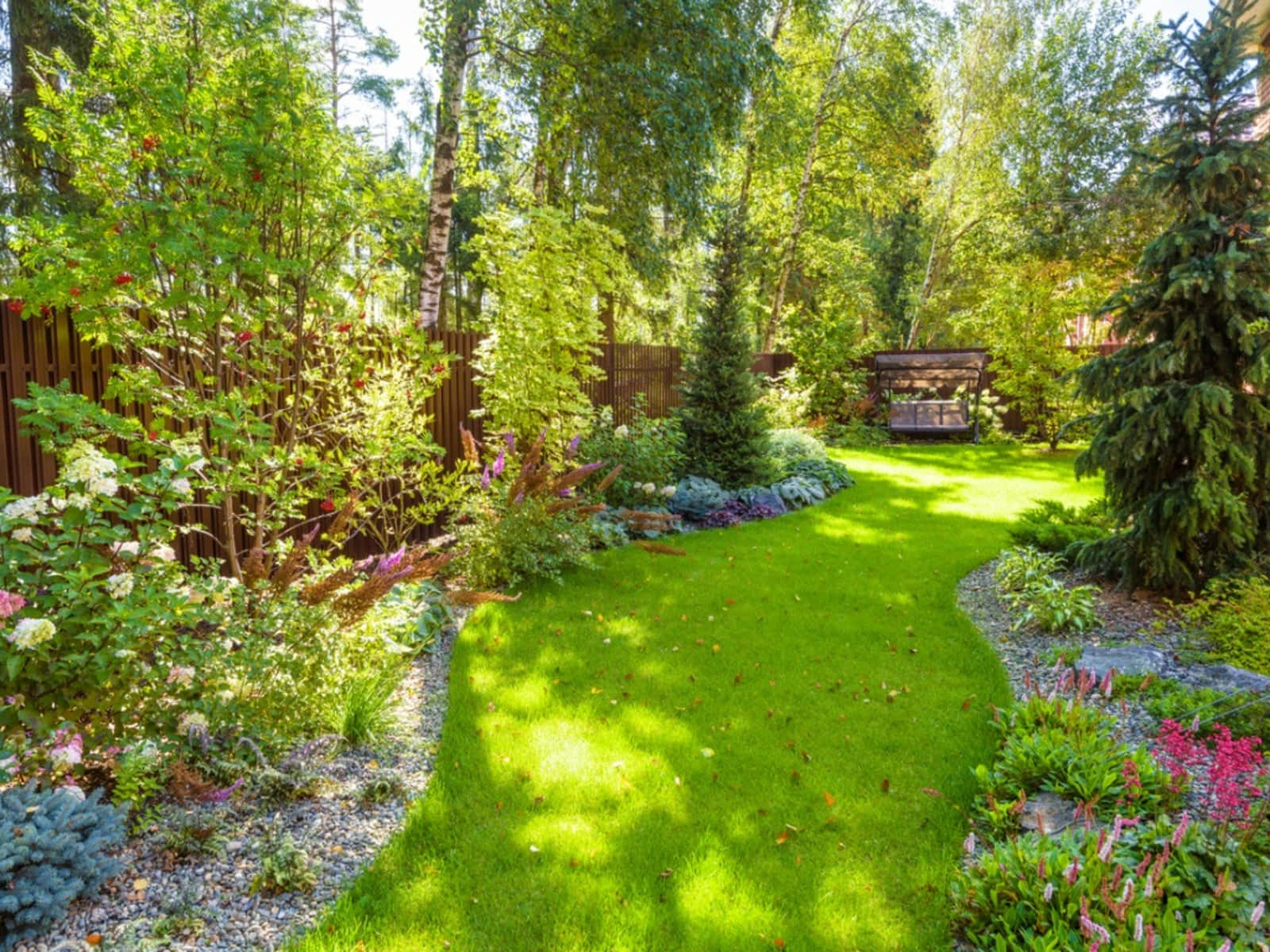 Cottage Garden 桌布 壁紙 — 一條陽光普照的花園小徑蜿蜒穿過充滿活力的綠色草地和色彩繽紛的花壇，兩旁鋪有礫石和高大的樹木。