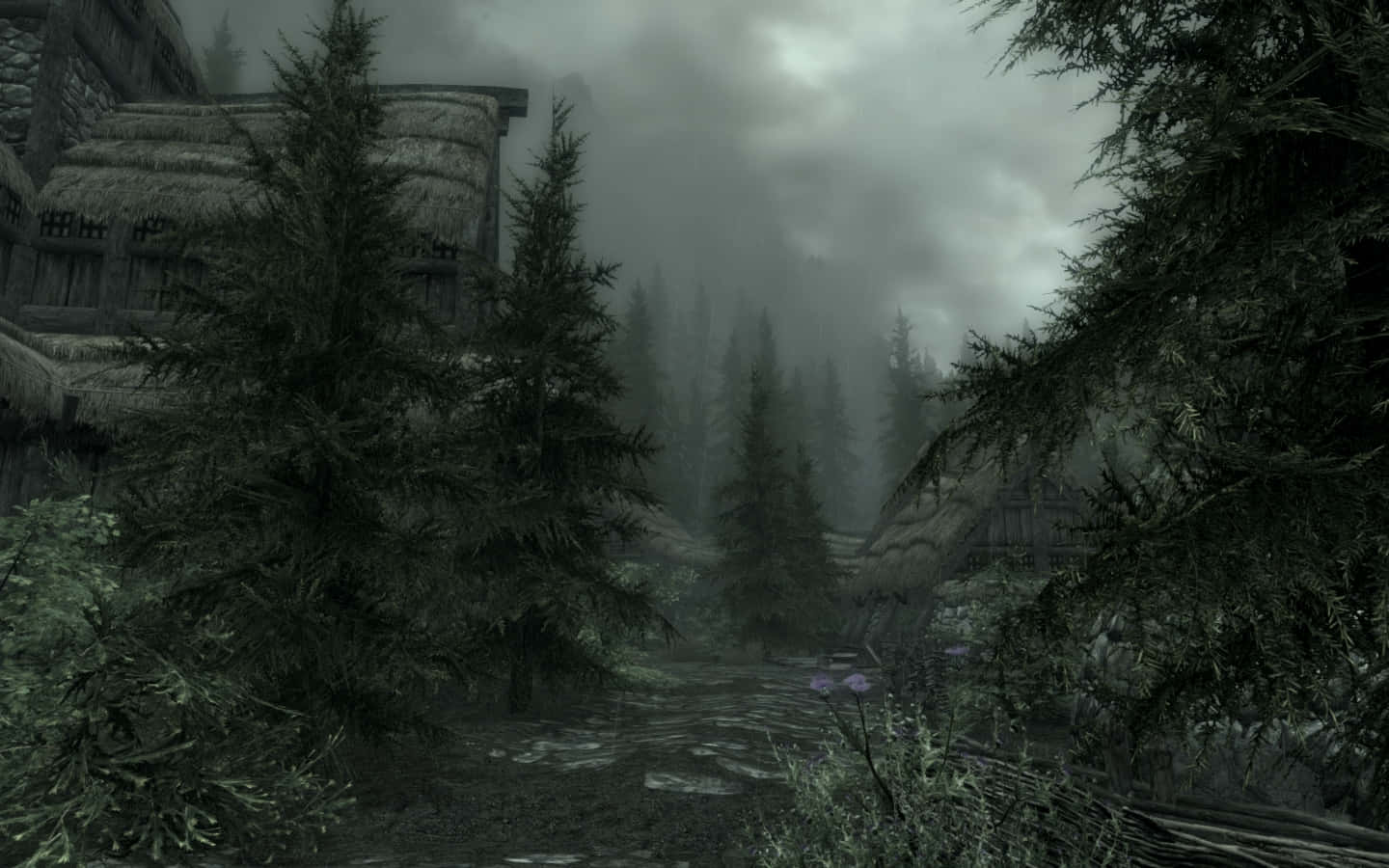 Skyrim Falkreath 桌布 壁紙 — 一條霧氣瀰漫的森林小徑蜿蜒經過古老的石屋，屋頂覆蓋著茅草，天空陰沉多雲。