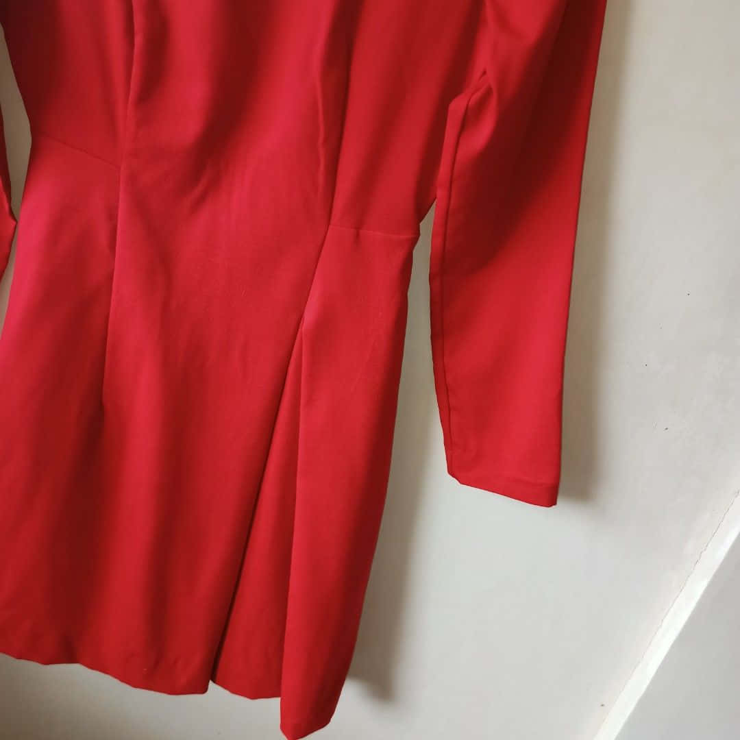 Red Clothing 桌布 壁紙 — 一條鮮豔的紅色連衣裙掛在純白色的牆上，展示其光滑的面料和量身定制的輪廓。