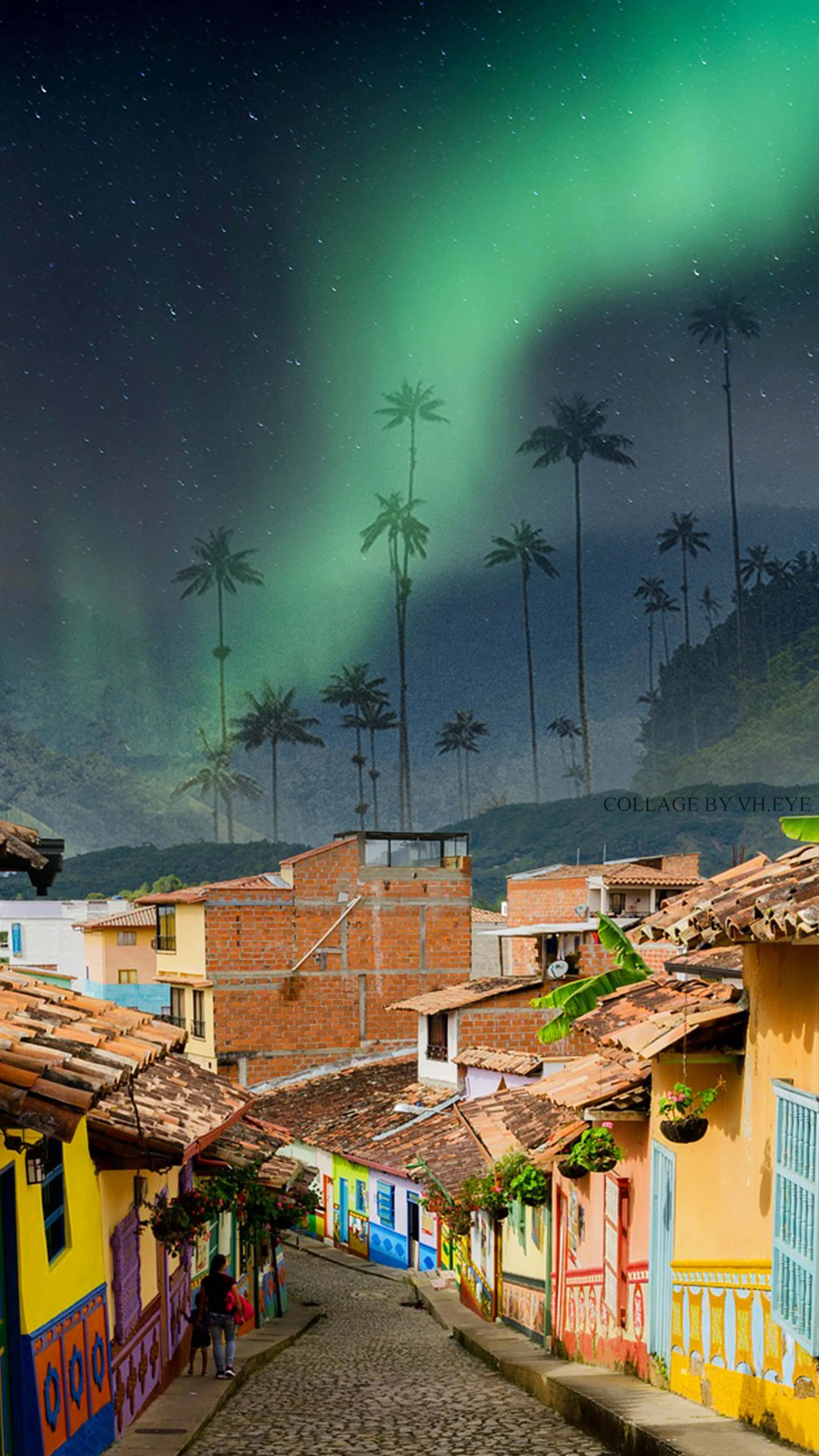 Colombia 桌布 壁紙 — 一條鵝卵石街道，兩旁是色彩繽紛的房屋，上方是星空，還有綠色極光和高大的棕櫚樹。