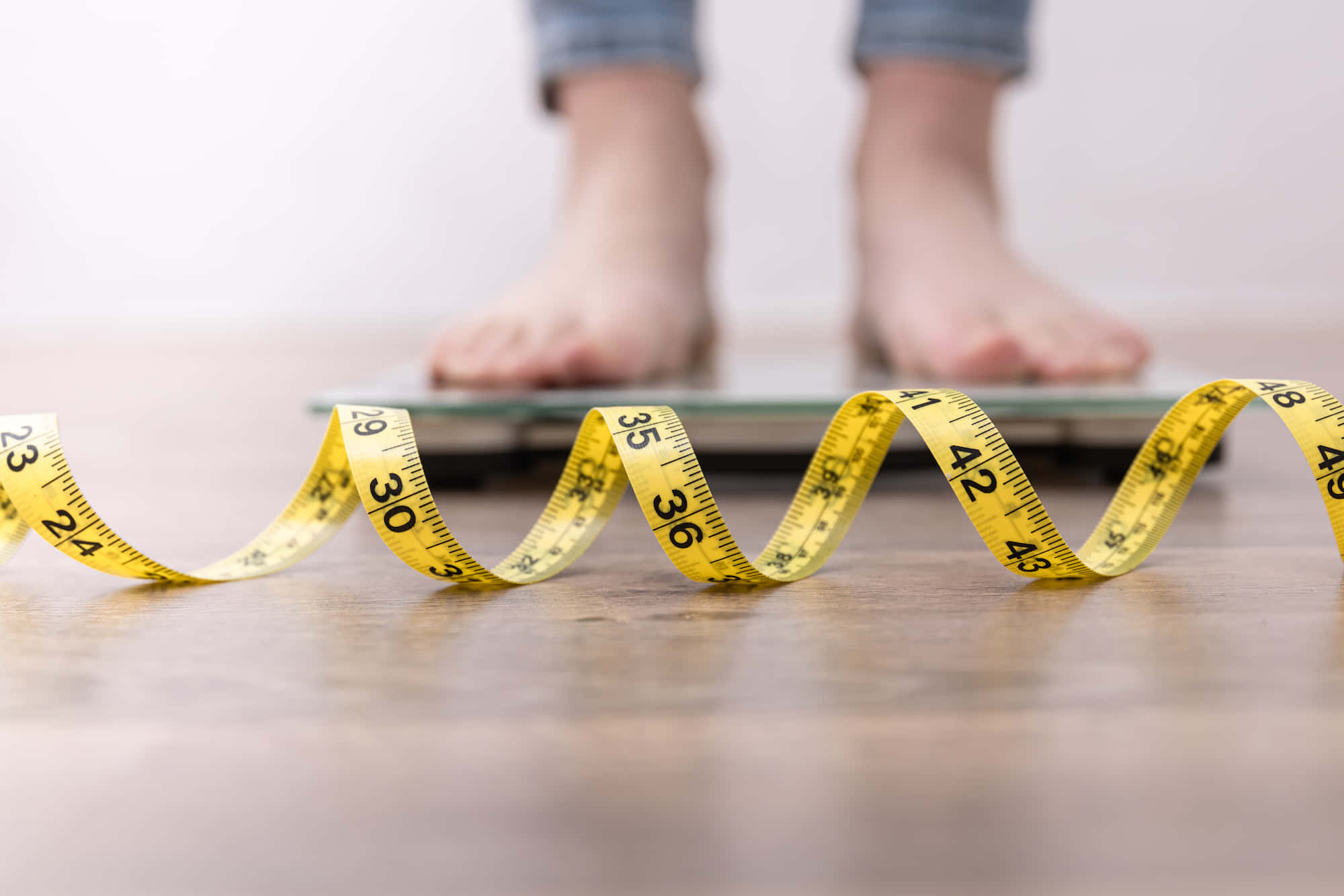 Weight Loss 桌布 壁紙 — 一條黃色軟尺在木地板上盤繞，前面有一雙赤腳站在電子磅上。