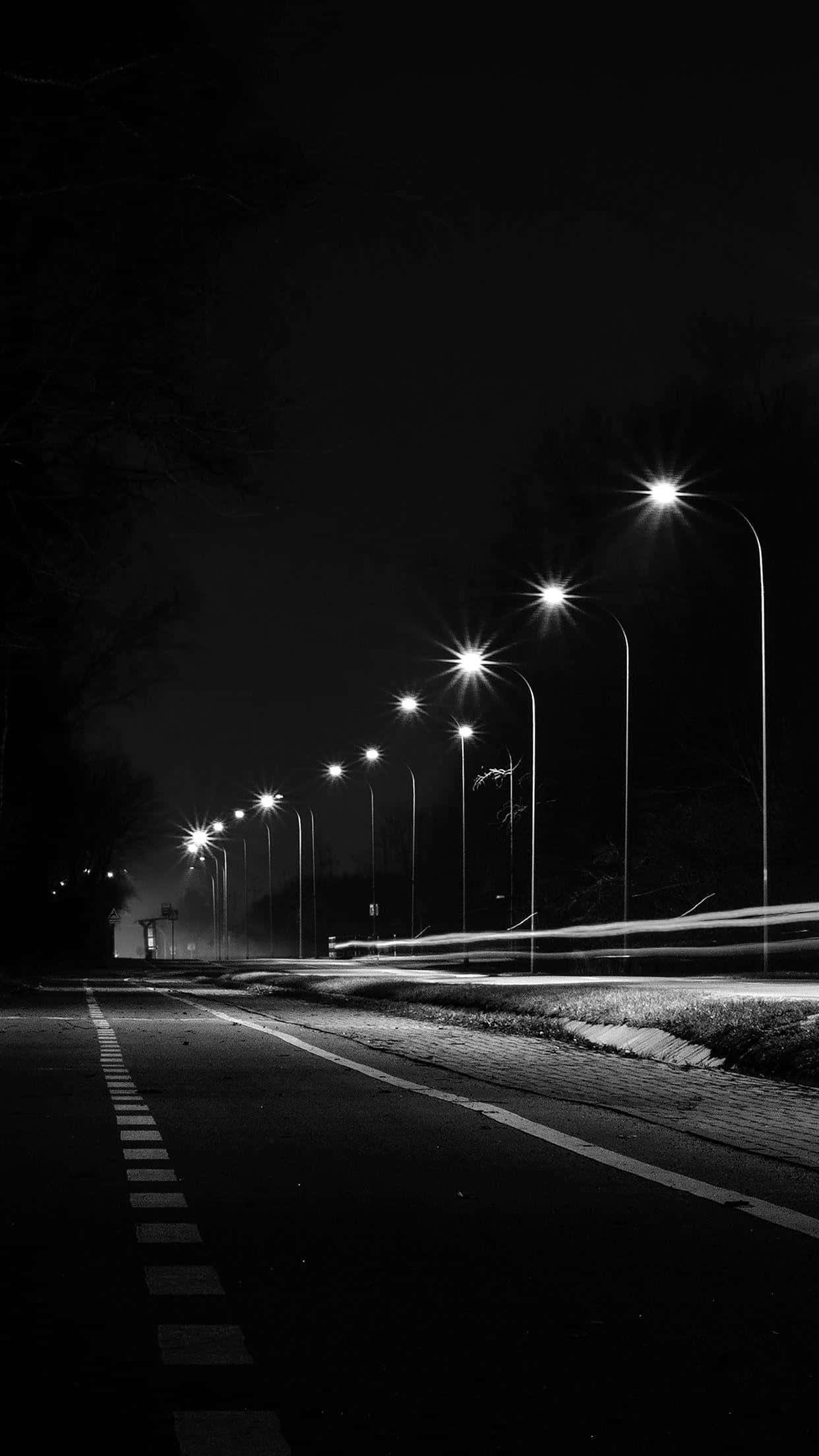 Black And White Street 桌布 壁紙 — 一條黑白夜景道路，兩旁街燈發出刺眼光芒，並有行駛中汽車造成的動態模糊。