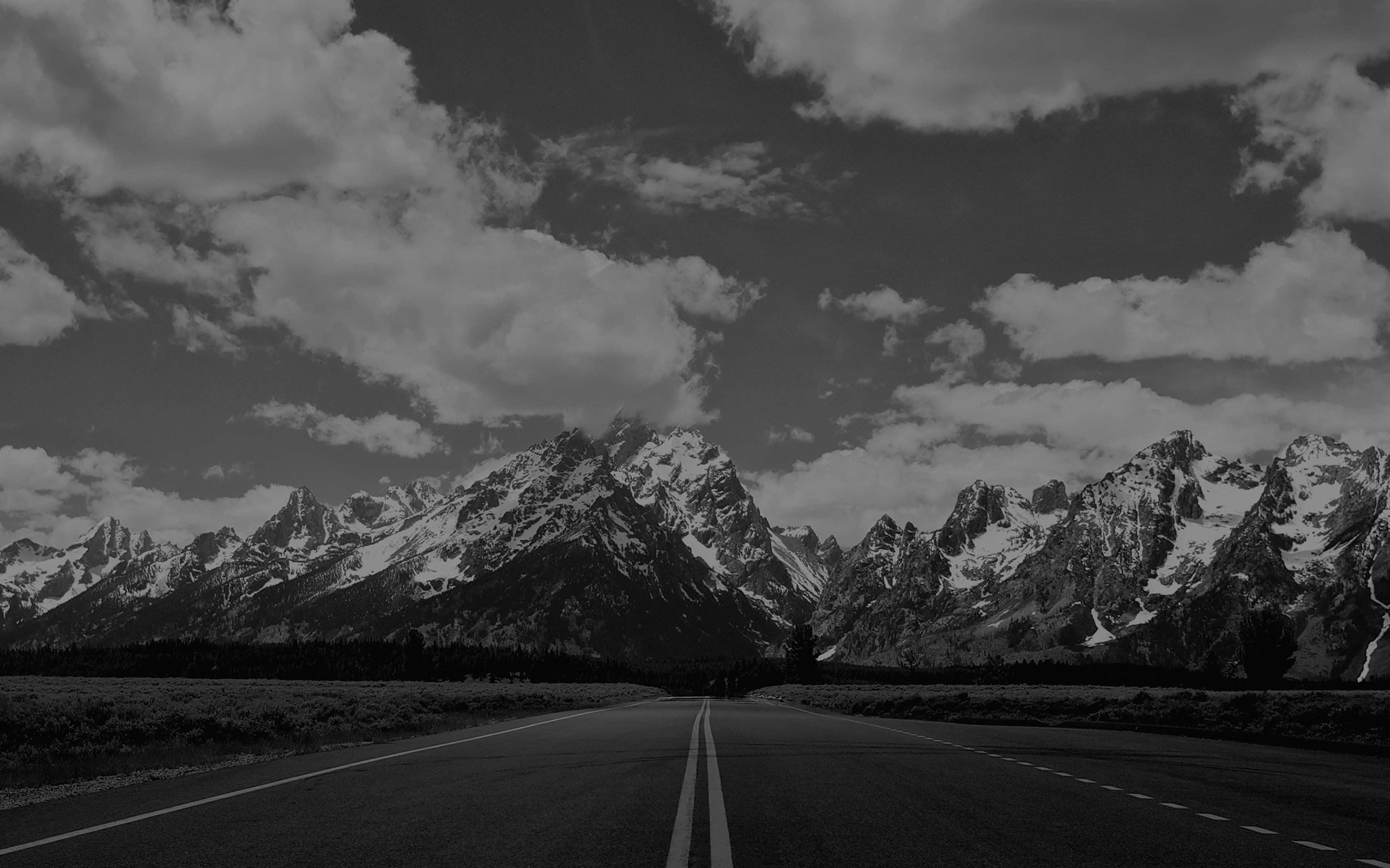 Black And White Nature 桌布 壁紙 — 一條黑白相間的道路在戲劇性的多雲天空下延伸向積雪的山峰。