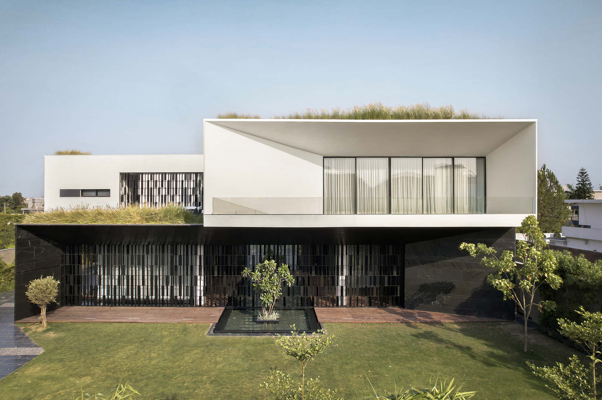 Minimalist Architecture 桌布 壁紙 — 一棟現代白色房屋，擁有綠色屋頂和黑色板條外牆，矗立在修剪整齊的草坪上，天空清澈湛藍。