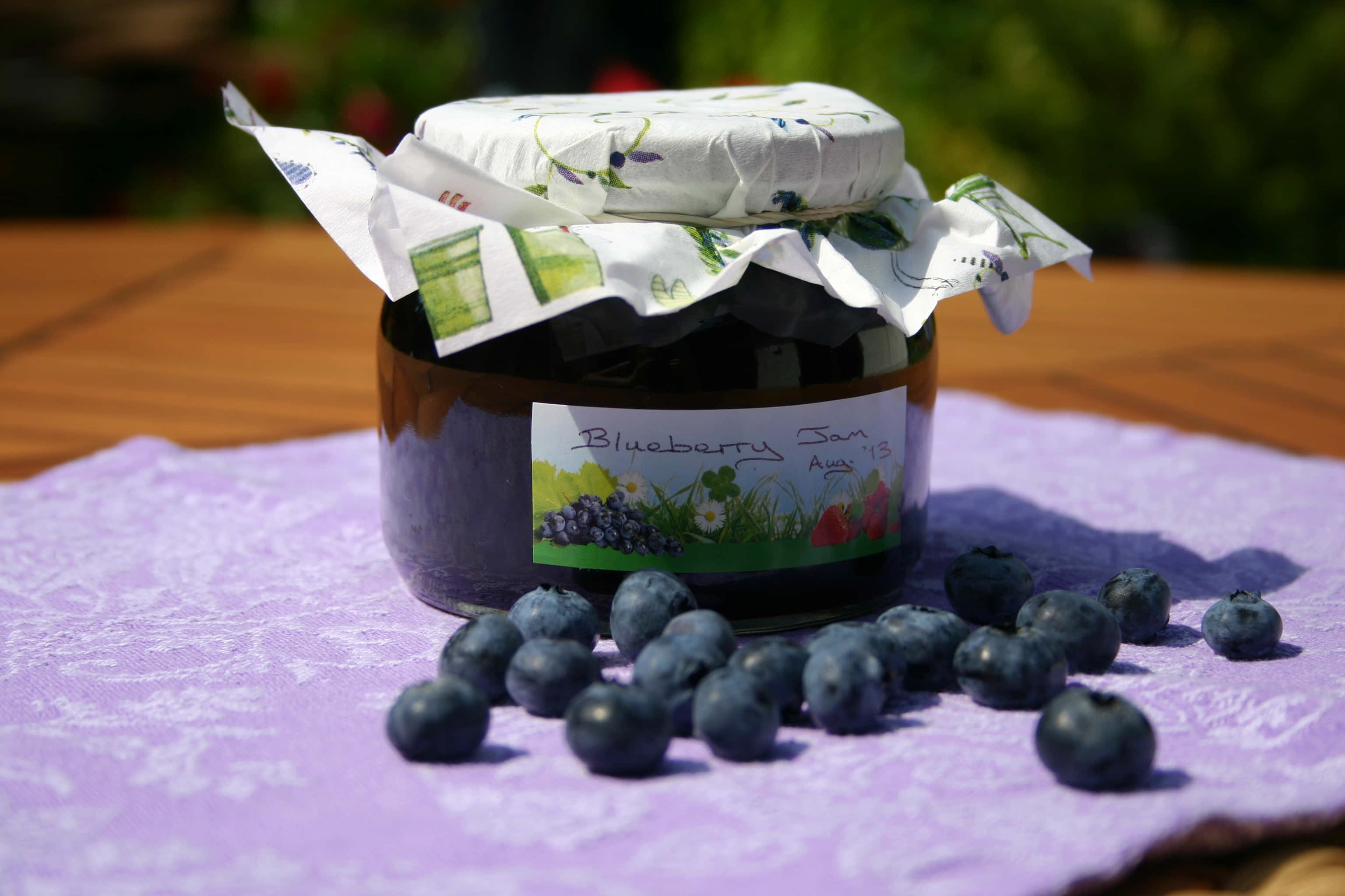 Blueberry Jam 桌布 壁紙 — 一樽自製藍莓醬配新鮮莓果放在紫色布上，在明亮陽光下。