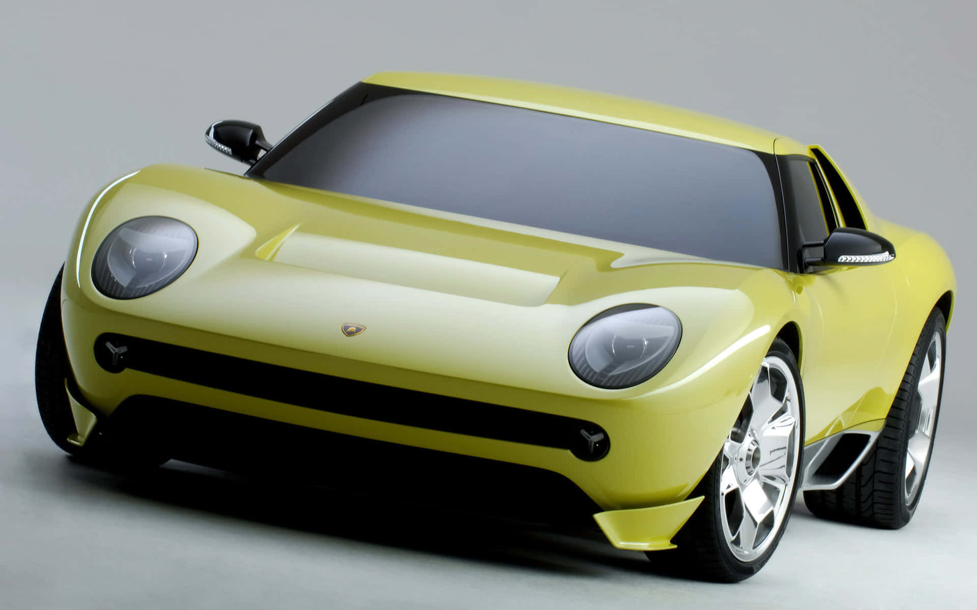 Lamborghini Miura 桌布 壁紙 — 一款時尚的黃色林寶堅尼概念車，配備圓形頭燈和銀色輪圈，在灰色中性工作室背景前展示。
