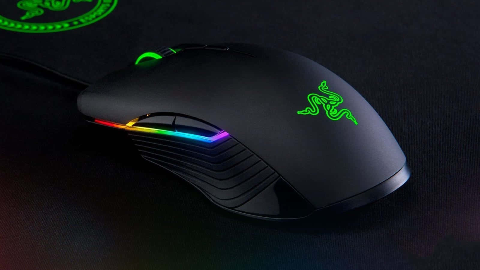 Gaming Mice 桌布 壁紙 — 一款時尚的黑色Razer遊戲滑鼠，帶有鮮豔的彩虹RGB燈光，放置在帶有發光綠色品牌的深色表面上。