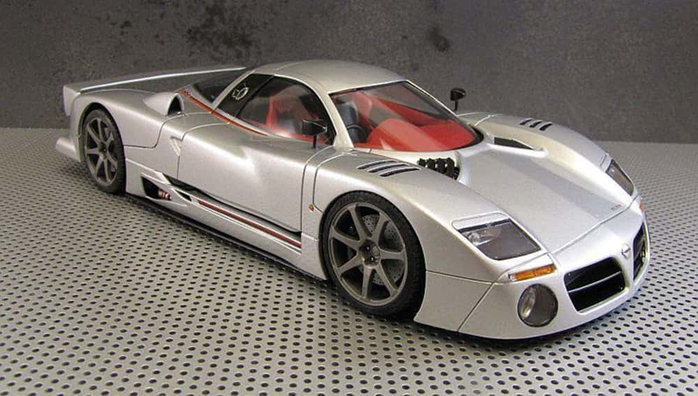 Car Model 桌布 壁紙 — 一款流線型銀色跑車模型，紅色內飾，放置在穿孔金屬表面上，背景為灰色牆壁。