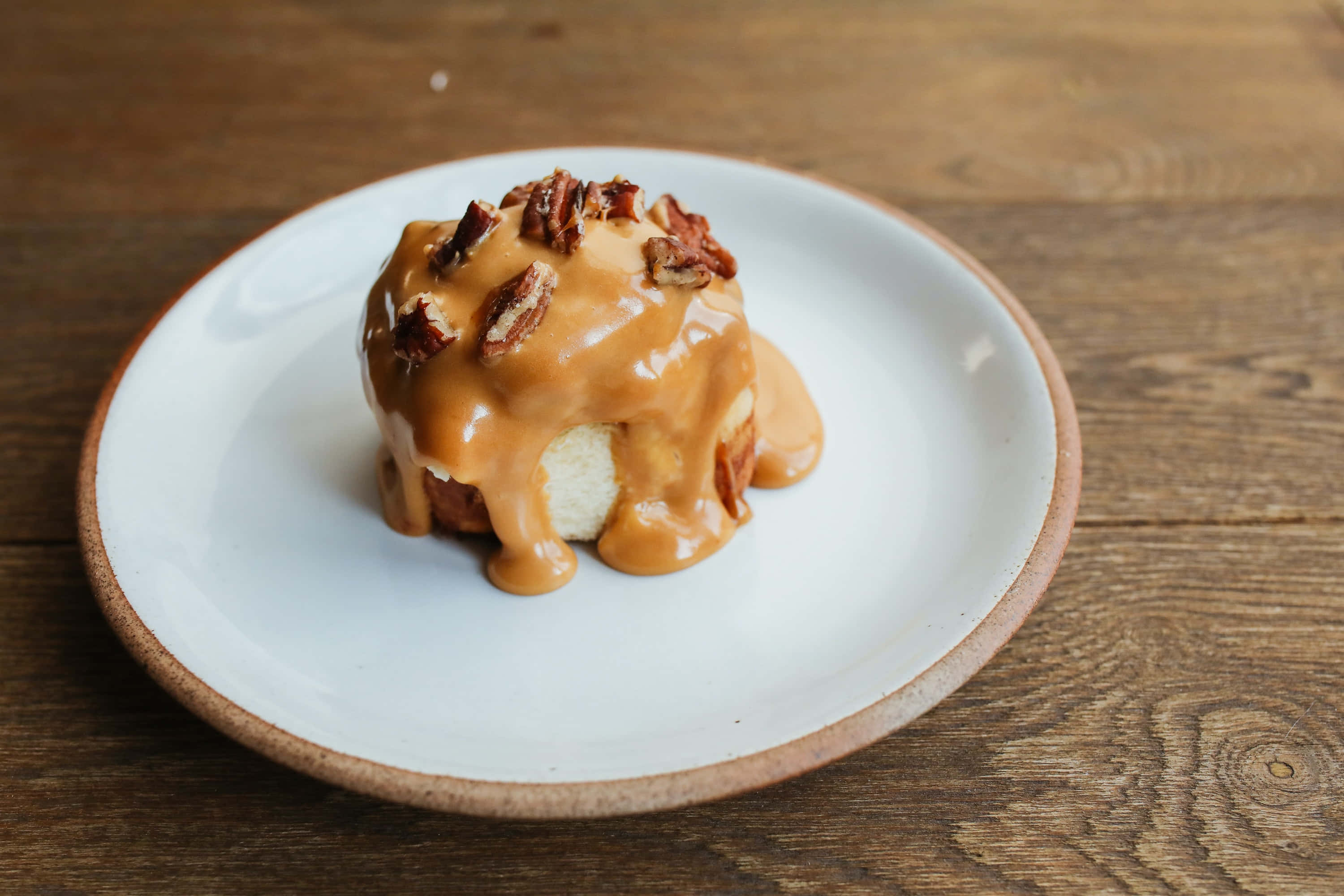 Caramel 桌布 壁紙 — 一款淋上焦糖、撒上碧根果的甜品，放在白色碟子上，置於鄉村風木桌上。