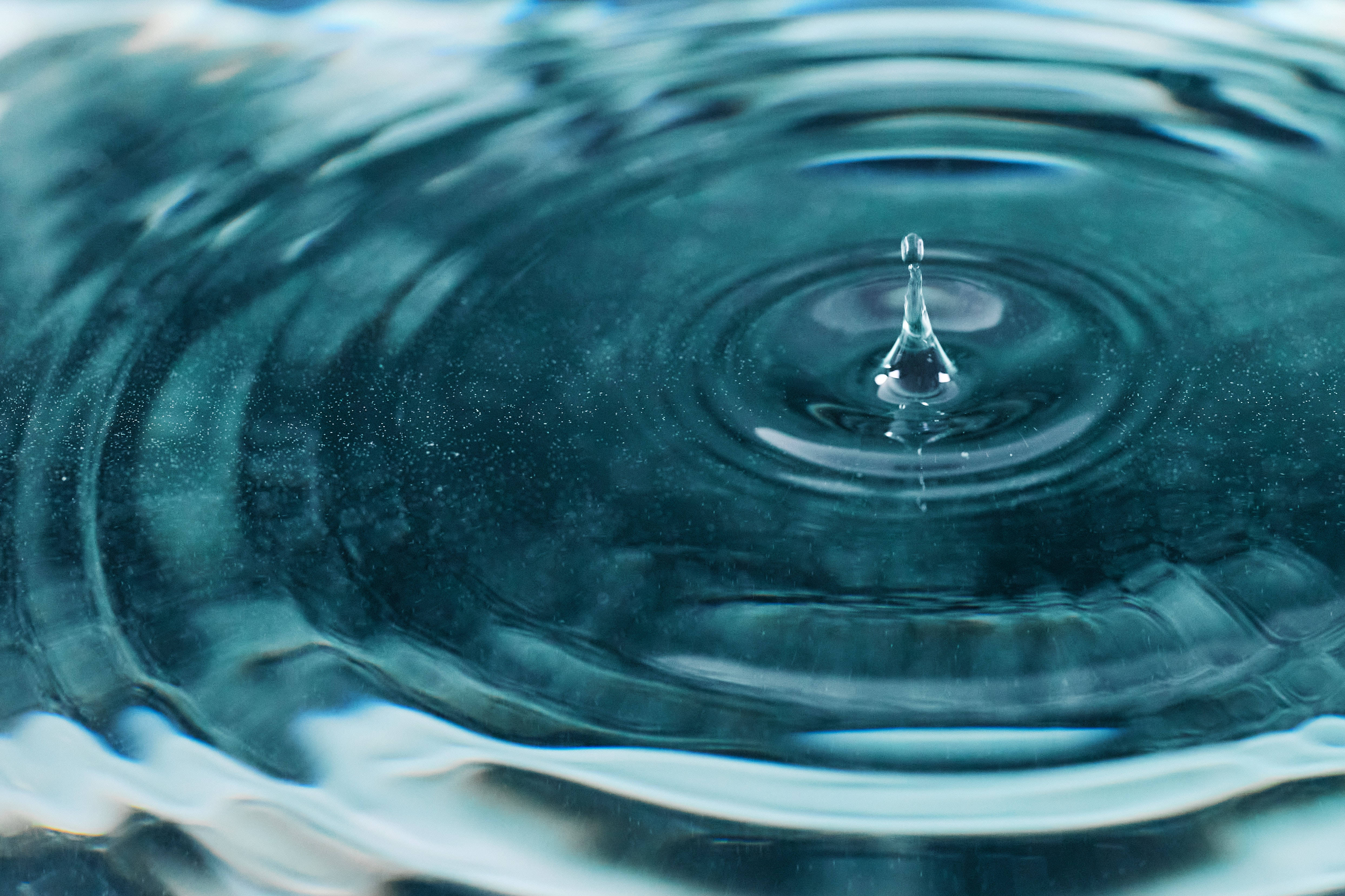 Water Drop 桌布 壁紙 — 一滴水懸浮在水面上，在清涼的藍色水中產生同心漣漪。