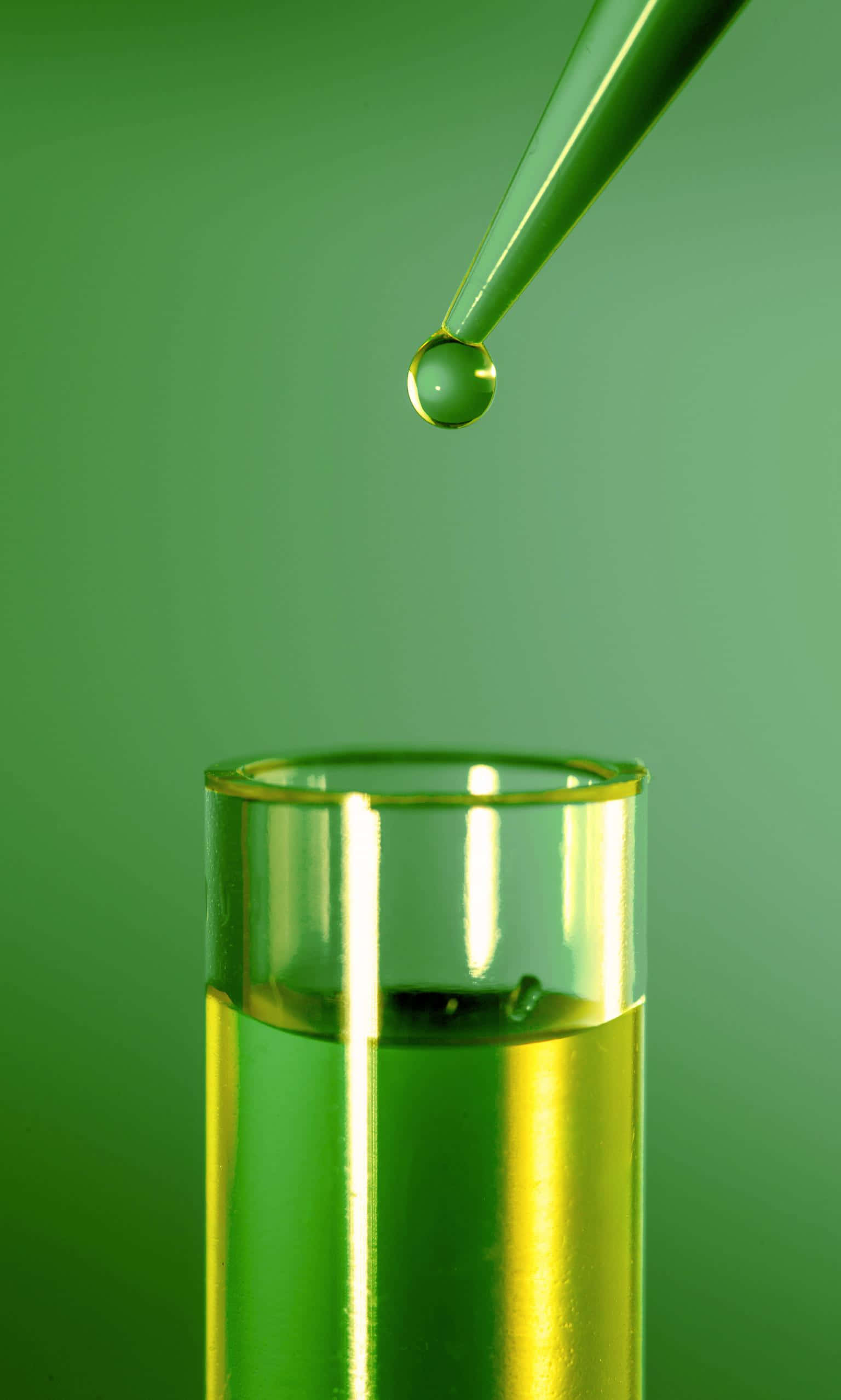 Green Chemistry 桌布 壁紙 — 一滴綠色液體懸浮在裝滿綠色液體的試管上方，背景為純綠色。