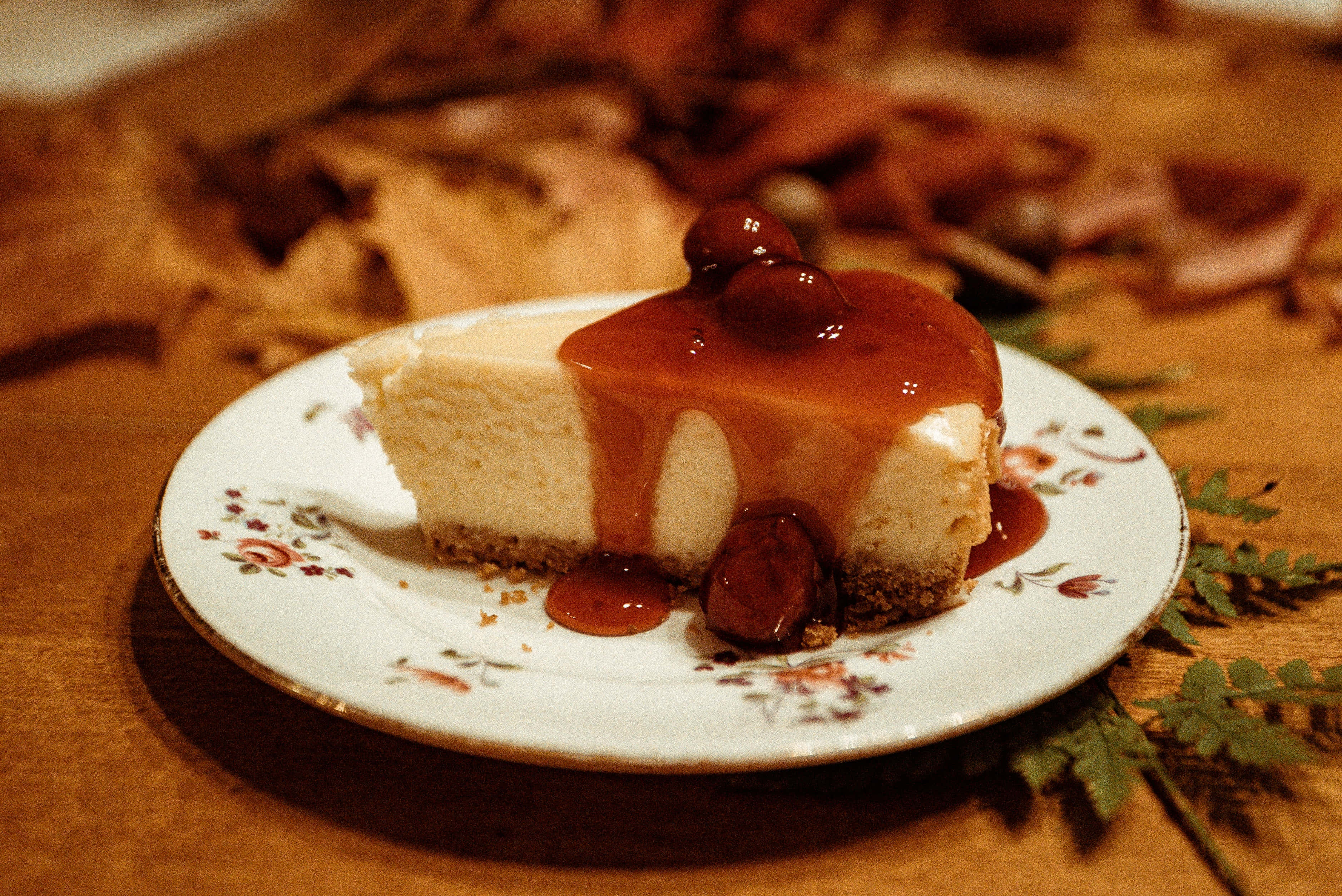 Caramel 桌布 壁紙 — 一片 creamy 芝士蛋糕，上面鋪滿光澤的櫻桃醬和整顆櫻桃，放在花卉圖案的碟子上，襯以溫暖的木質背景。