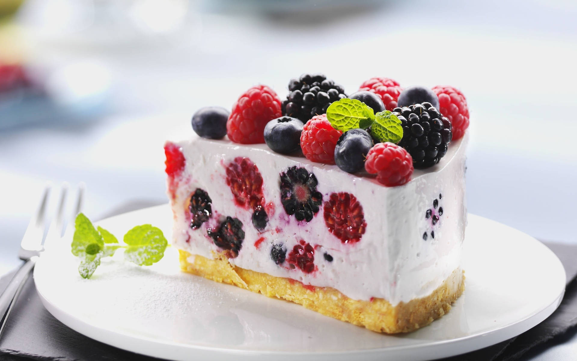 Berry 桌布 壁紙 — 一片 creamy 莓果芝士蛋糕，上面鋪滿新鮮紅桑子、黑莓和藍莓，並以薄荷葉點綴，放在白色碟子上。