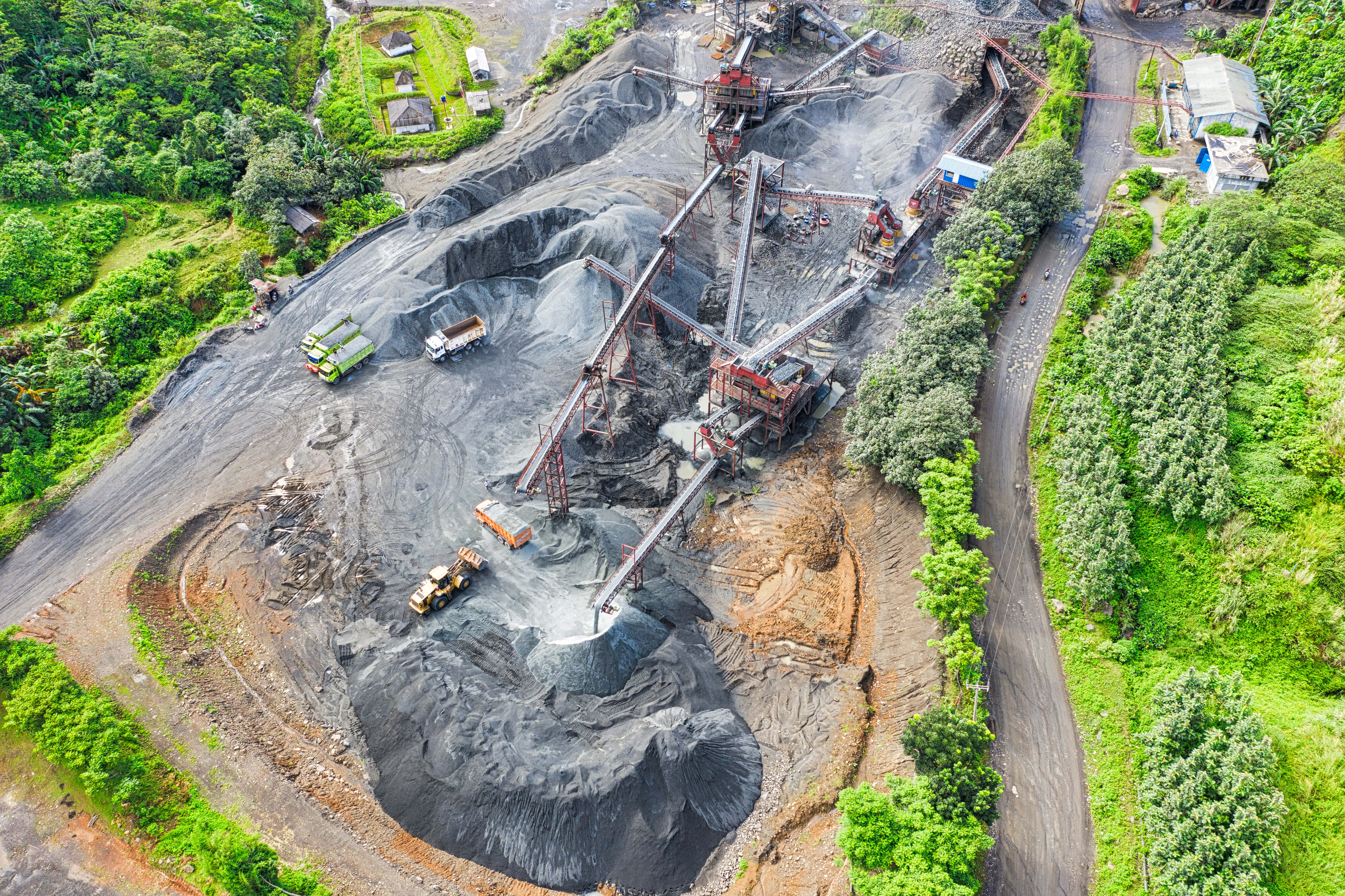 Mining 桌布 壁紙 — 一片廣闊的露天煤礦的鳥瞰圖，其中有輸送帶、卡車和機械，周圍環繞著茂密的綠色森林。