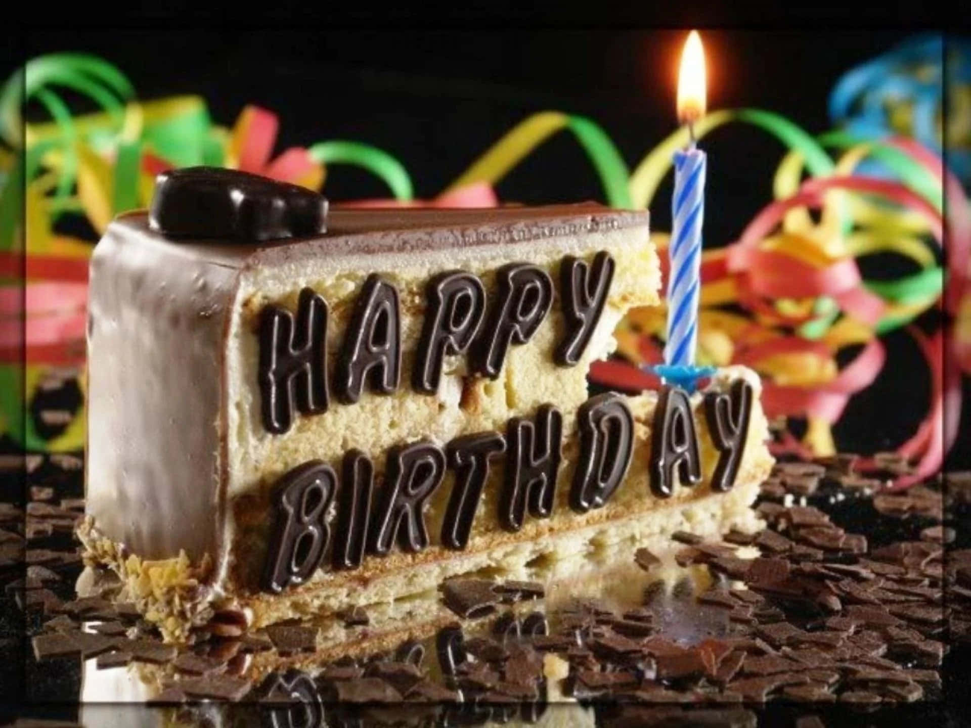生日蛋糕 桌布 壁紙 — 一片朱古力生日蛋糕，上面有朱古力字母寫成的「生日快樂」和一支點燃的蠟燭，周圍環繞著色彩繽紛的彩帶。