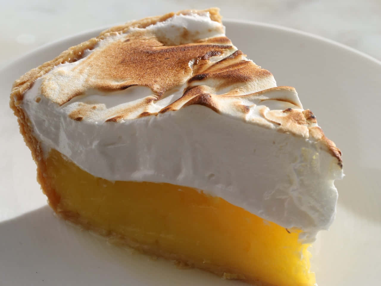 Meringue 桌布 壁紙 — 一片檸檬蛋白批，上面有烤過的蛋白霜，放在白色碟子上，在明亮日光下。