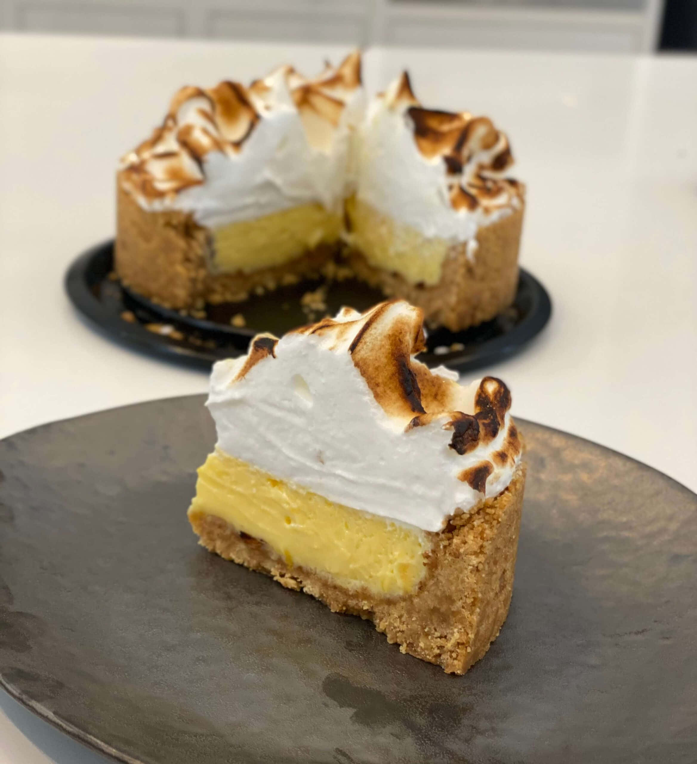 Meringue 桌布 壁紙 — 一片檸檬蛋白派，上面有烤過的蛋白霜，放在深色盤子上，背景中其餘的派模糊不清。