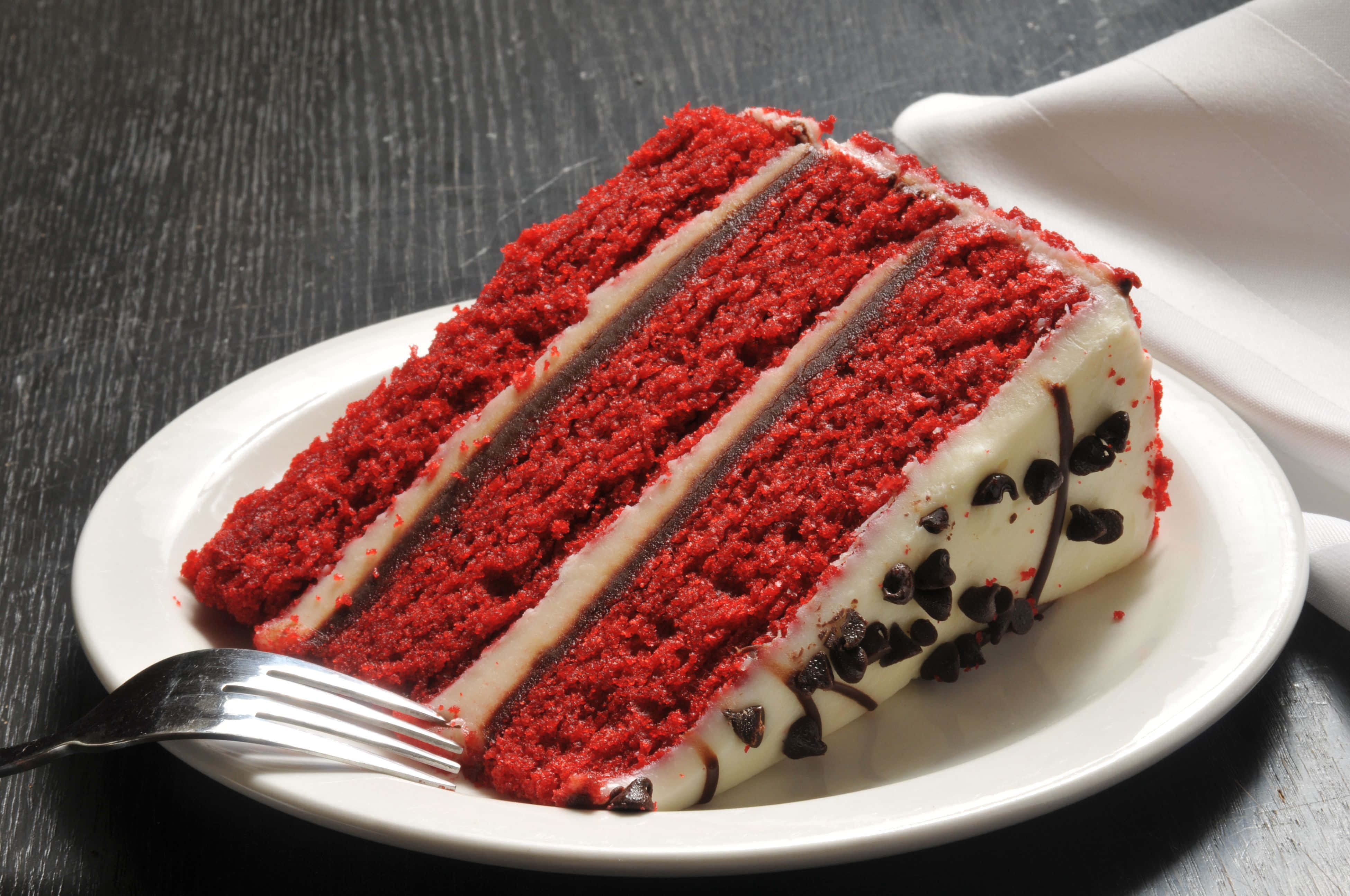 Red Velvet Cake 桌布 壁紙 — 一片豐富的紅絲絨蛋糕，配上奶油芝士糖霜和朱古力淋醬，放在白色碟子上，旁邊有一把叉。