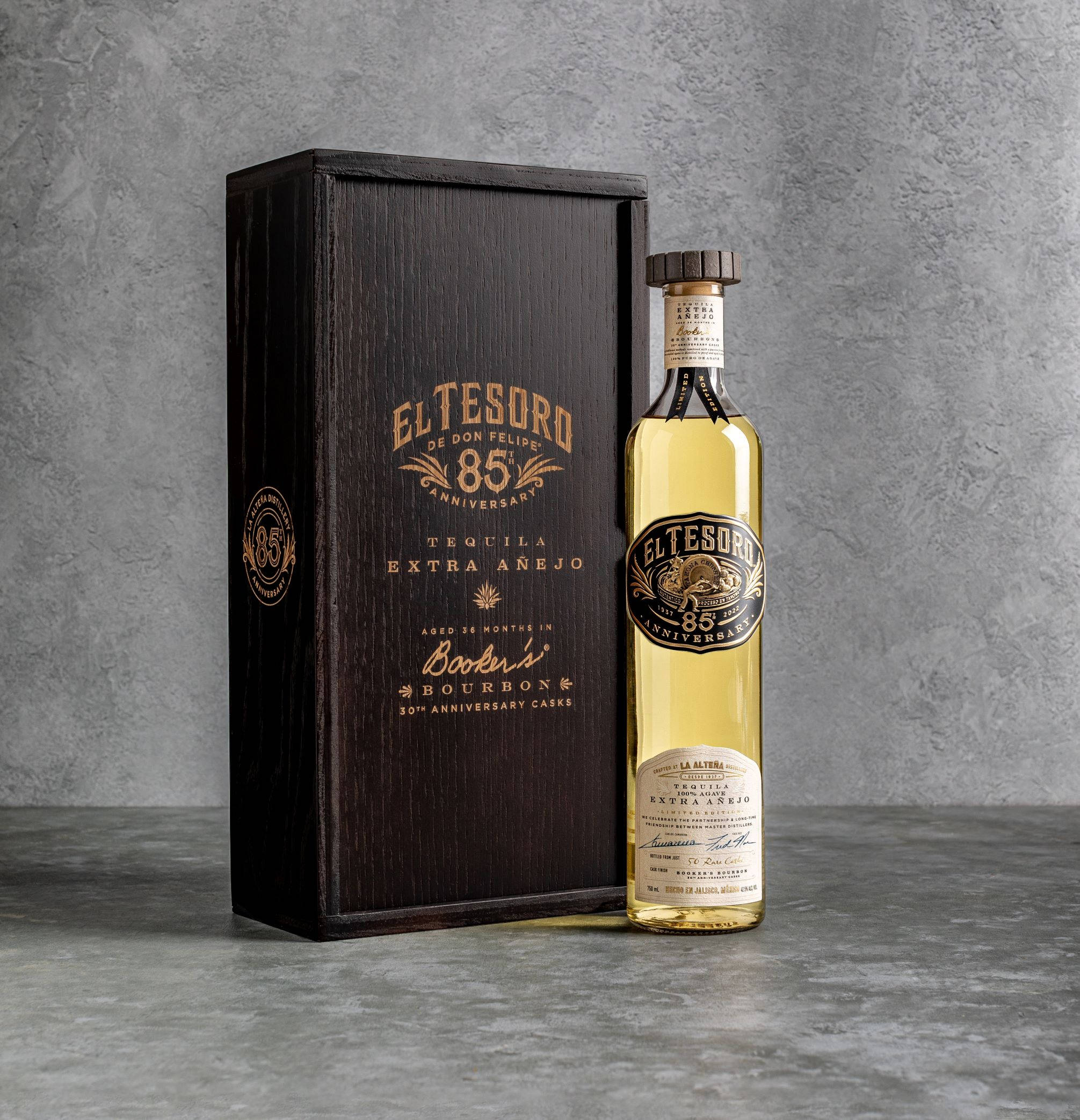 El Tesoro Extra Añejo Booker's Bourbon 壁紙 — 一瓶El Tesoro 85週年紀念特級陳年龍舌蘭酒，旁邊是其深色木盒，背景是紋理灰色混凝土牆。