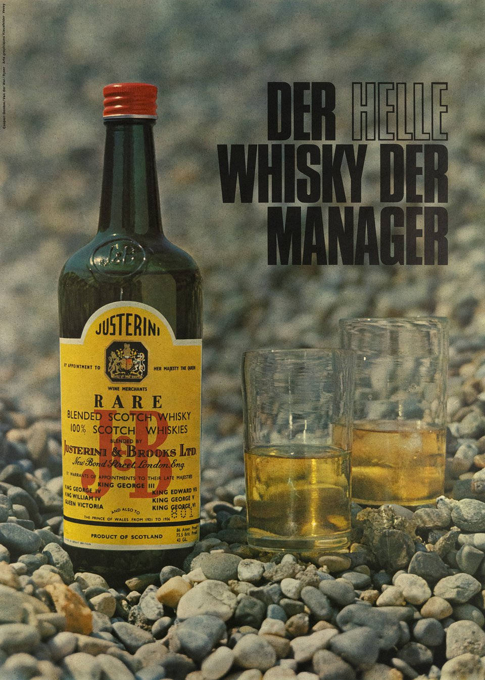 J&B Der Helle Whisky Der Manager 壁紙 — 一瓶復古的Justerini's威士忌和兩個玻璃杯放在卵石灘上，粗體德文文字宣告「Der Helle Whisky Der Manager」。