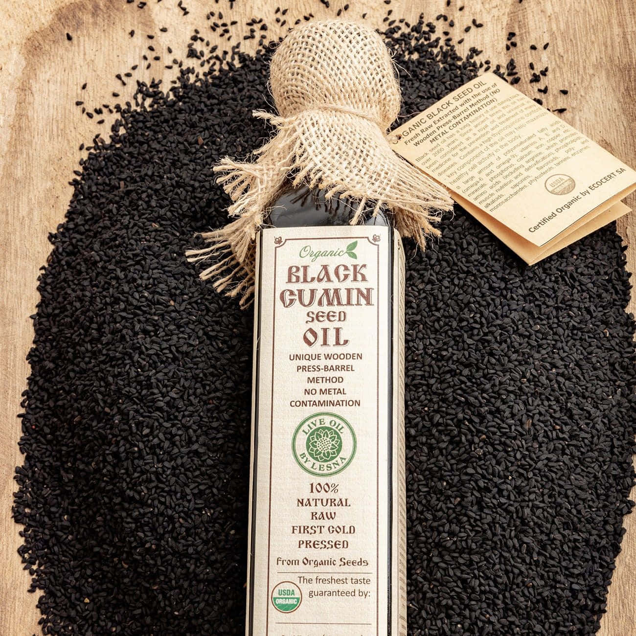 Black Cumin 桌布 壁紙 — 一瓶有機黑孜然籽油放在鄉村風木質表面上，底下鋪著黑色種子。