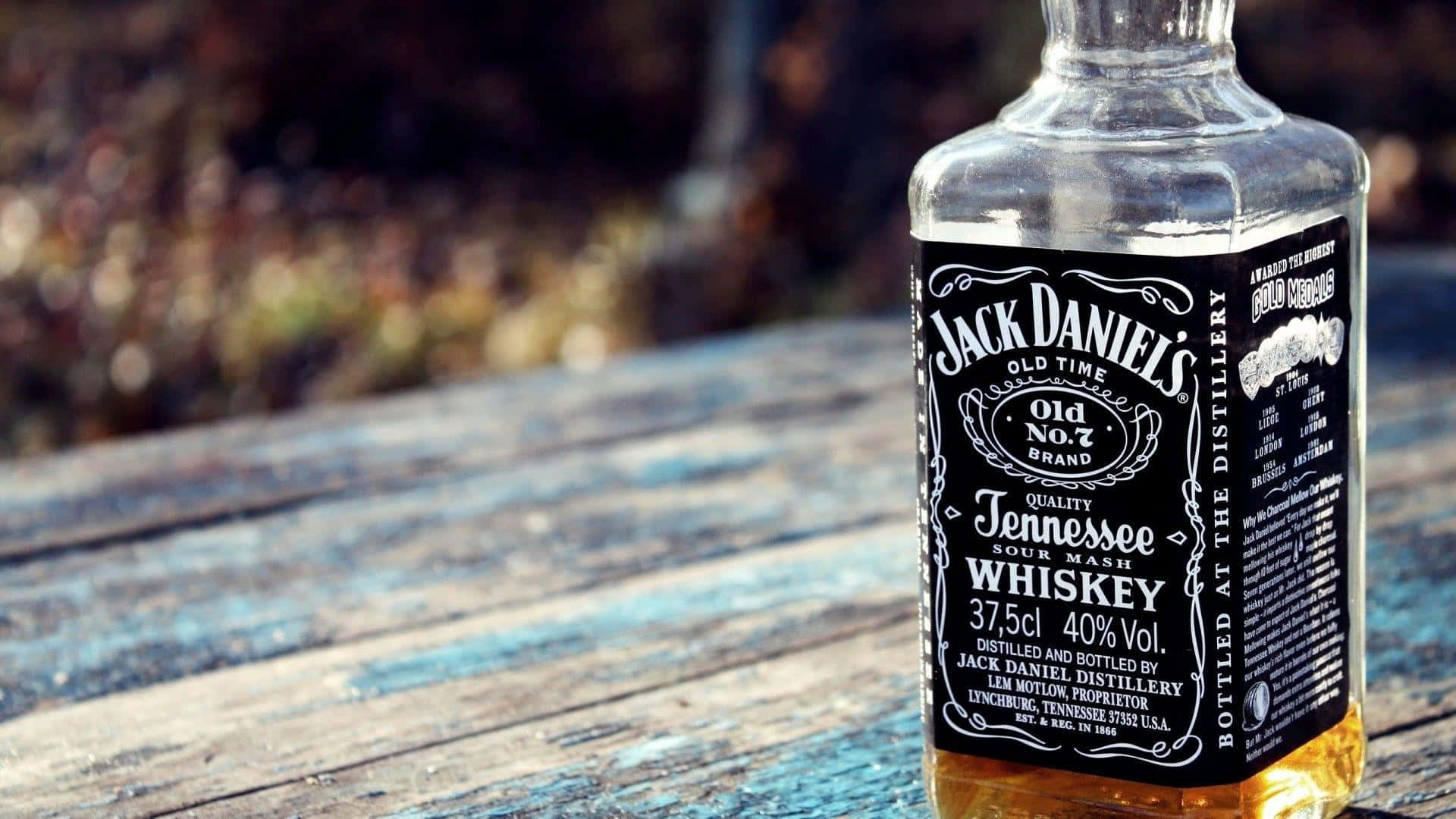 alcohol 桌布 壁紙 — 一瓶清澈的Jack Daniel's田納西威士忌放在一張風化的藍色木桌上，背景是模糊的秋葉。
