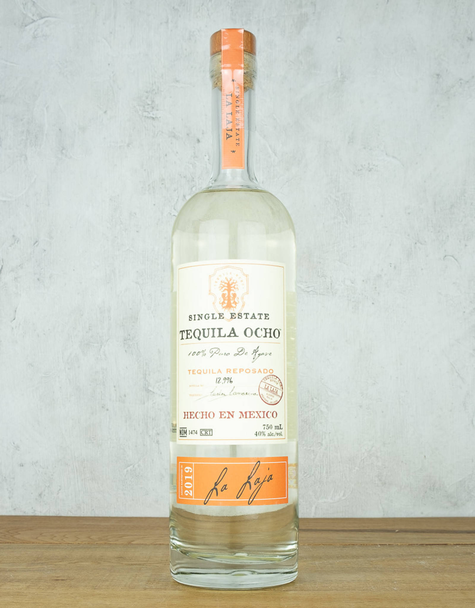 Tequila Ocho Reposado 750ml 壁紙 — 一瓶清澈的Tequila Ocho reposado直立於木質表面上，背景是帶紋理的灰色牆壁。