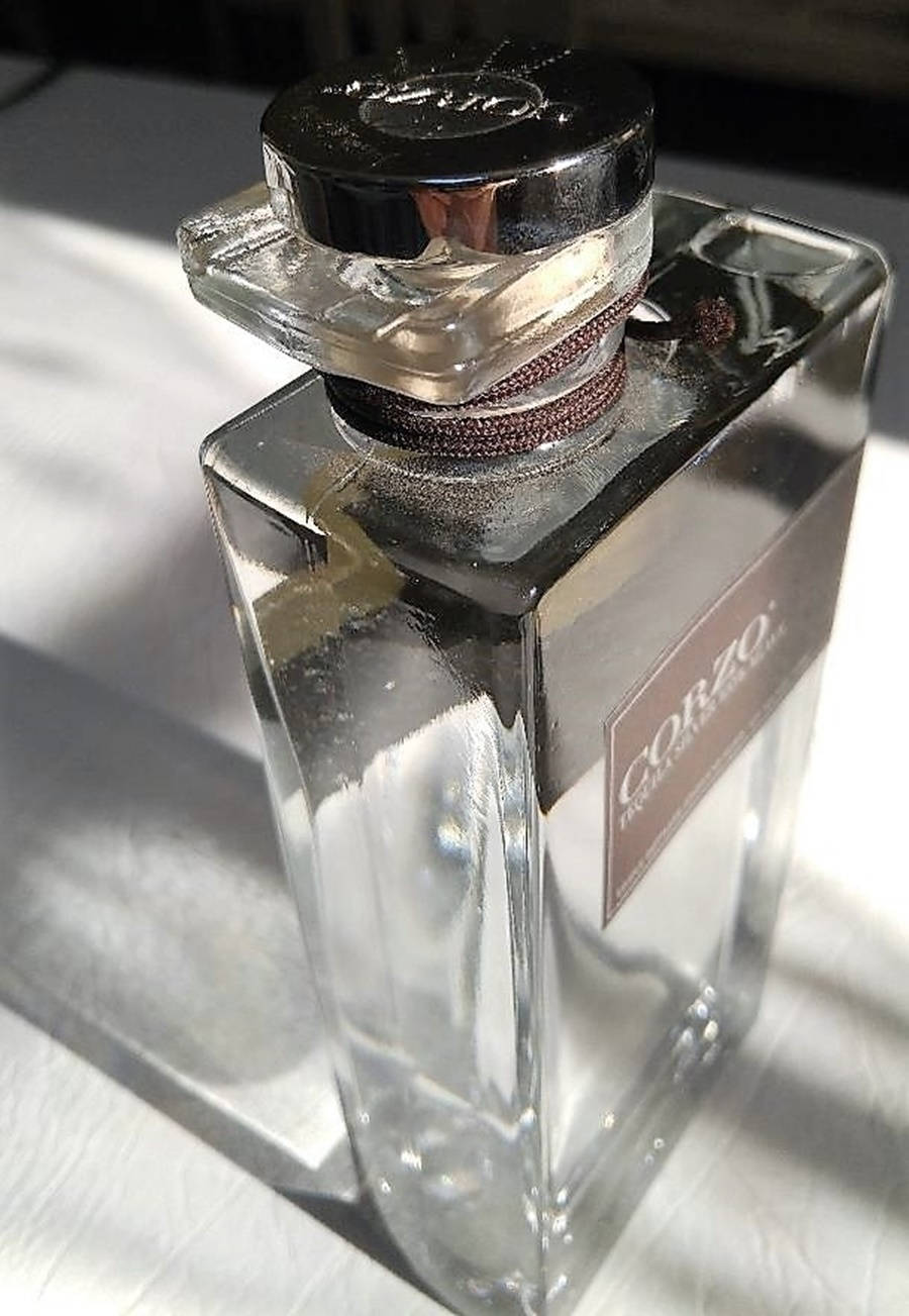 一個透明的玻璃香水瓶，帶有黑色瓶蓋和棕色標籤，在白色表面上。