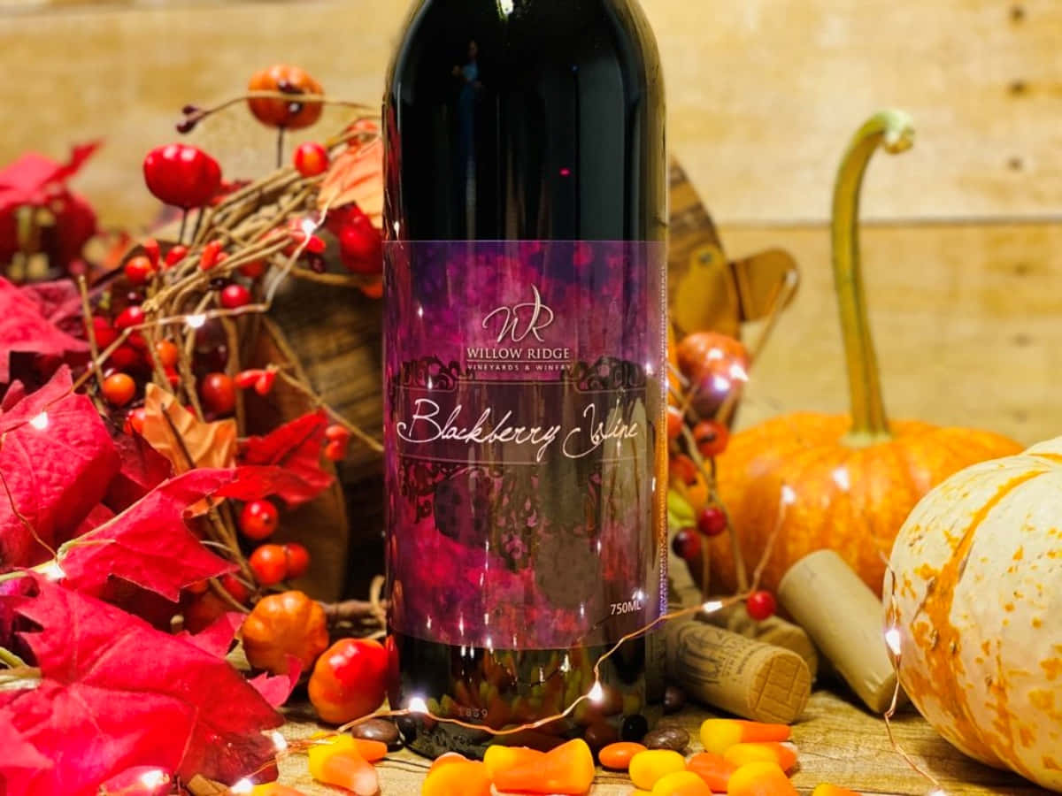 Blackberry Wine 桌布 壁紙 — 一瓶黑莓酒置於中央，周圍環繞著秋葉、南瓜和糖果玉米，在溫暖的仙女燈下。