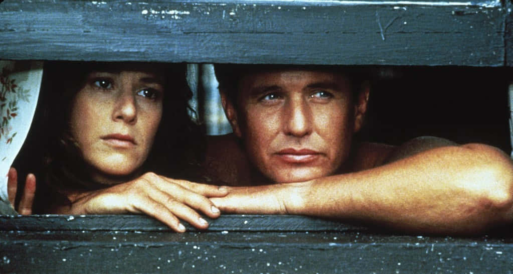 Tom Berenger 桌布 壁紙 — 一男一女透過一塊風化的木條專注地凝視，表情緊張而集中。