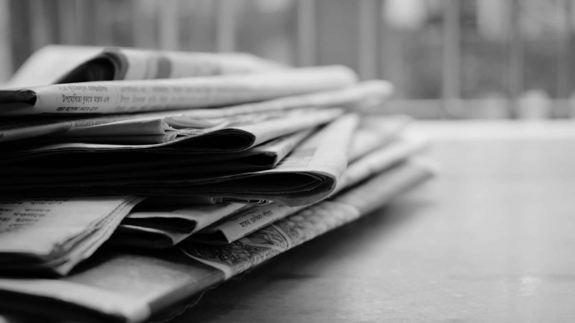 Black And White Newspaper 桌布 壁紙 — 一疊單色摺疊報紙放在光滑表面上，背景模糊。