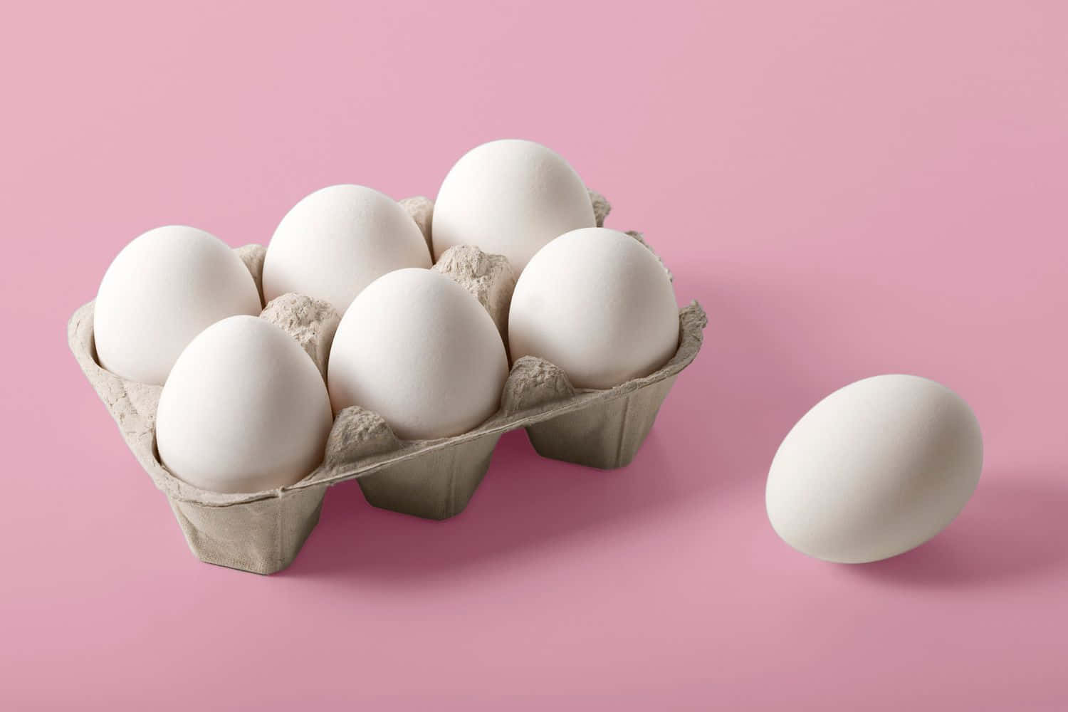Eggs 桌布 壁紙 — 一盒白色雞蛋放在柔軟的粉紅色背景上，旁邊放著一隻雞蛋。