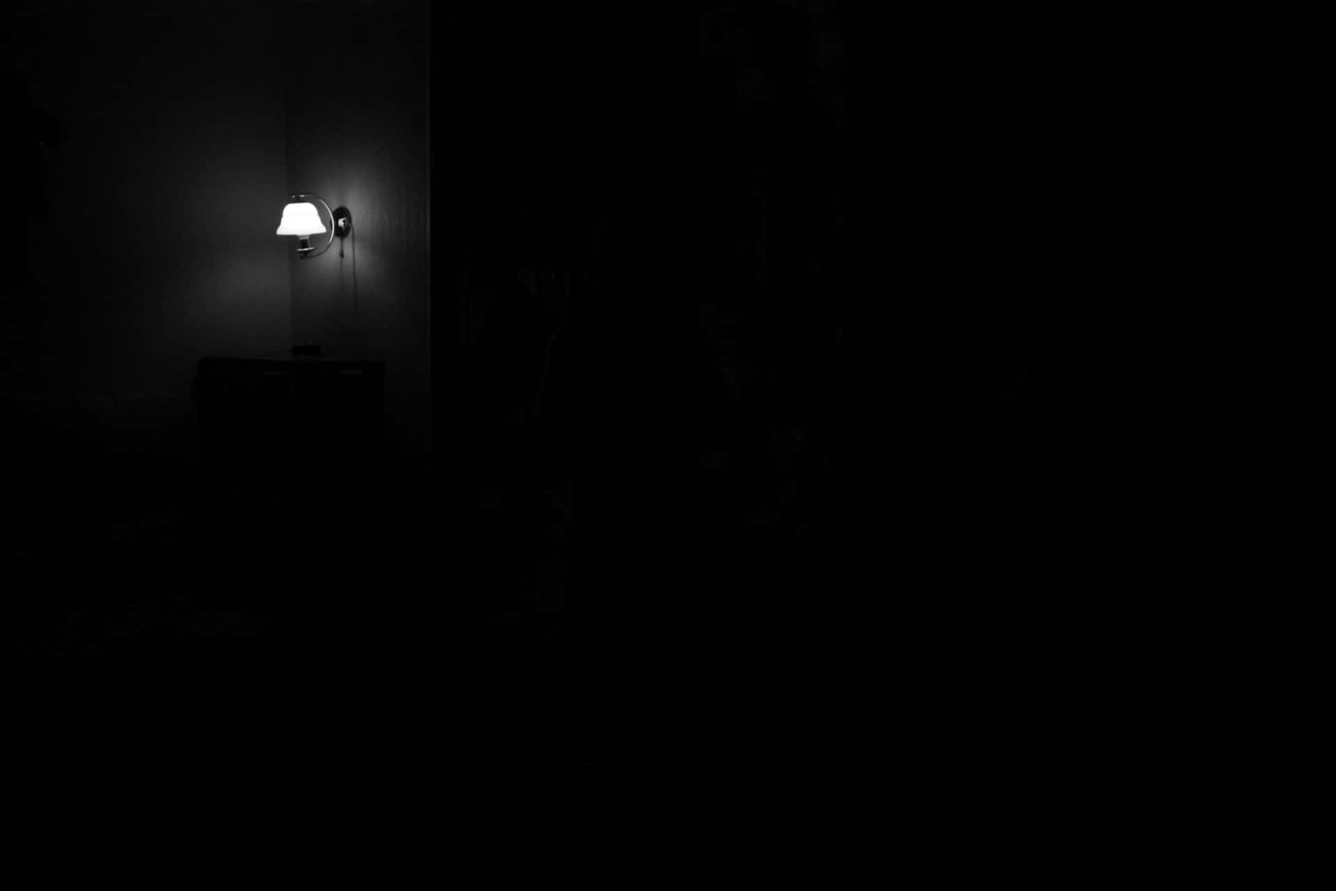 Dark Room 桌布 壁紙 — 一盞壁燈在漆黑的房間中發出柔和的光芒，營造出深邃的陰影。