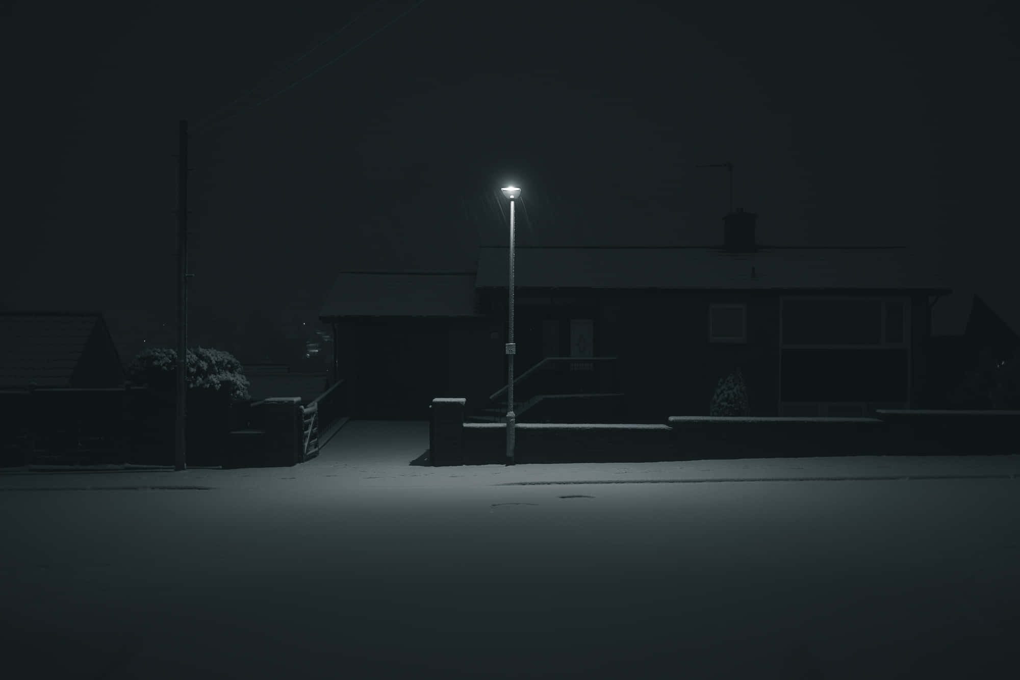 Dark Night 桌布 壁紙 — 一盞孤獨的路燈在夜晚將柔和的光芒投射在積雪的郊區街道上，照亮了黑暗中的寧靜房屋。