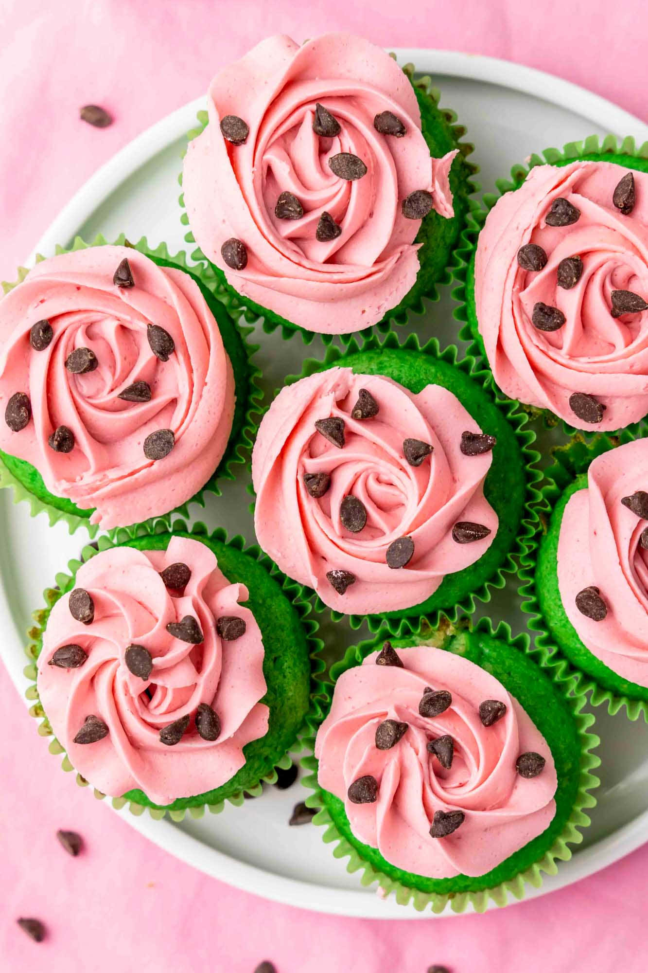 Pink Cupcakes 桌布 壁紙 — 一盤綠色紙杯蛋糕，上面有粉紅色玫瑰漩渦糖霜和朱古力碎，放在粉紅色背景上。