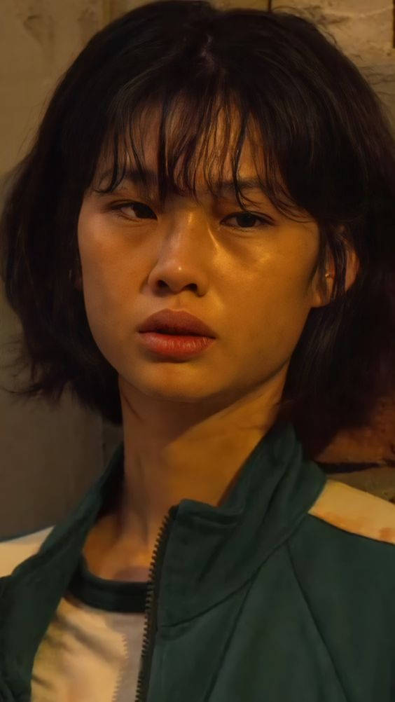 一瞥韓國善別克的壯麗風光 壁紙 — 一位年輕黑髮女子穿著綠色外套，在溫暖昏暗燈光下的特寫肖像。